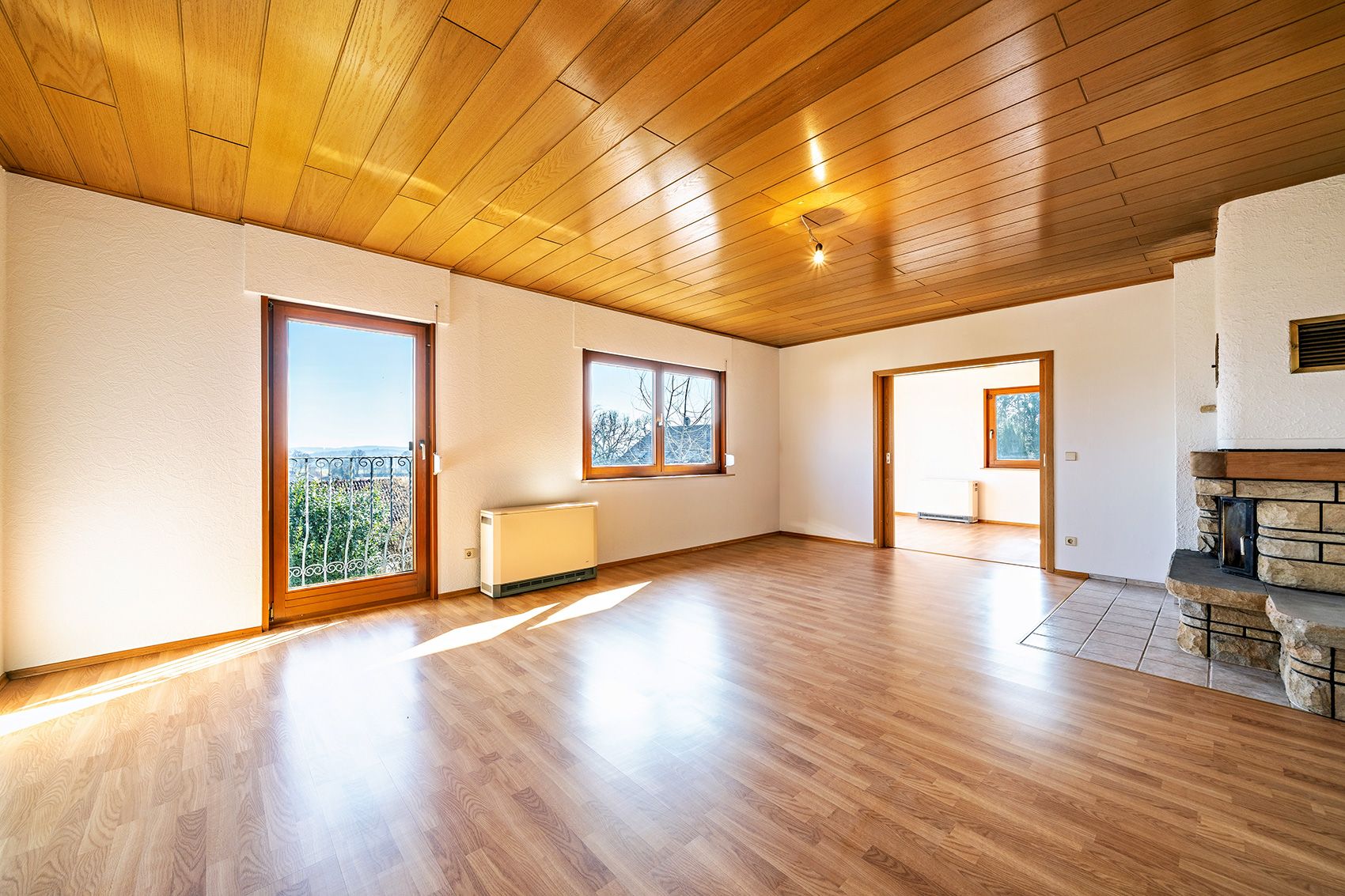 Helles Wohnzimmer mit Holzdecke, Parkettboden, Kamin und großen Fenstern.