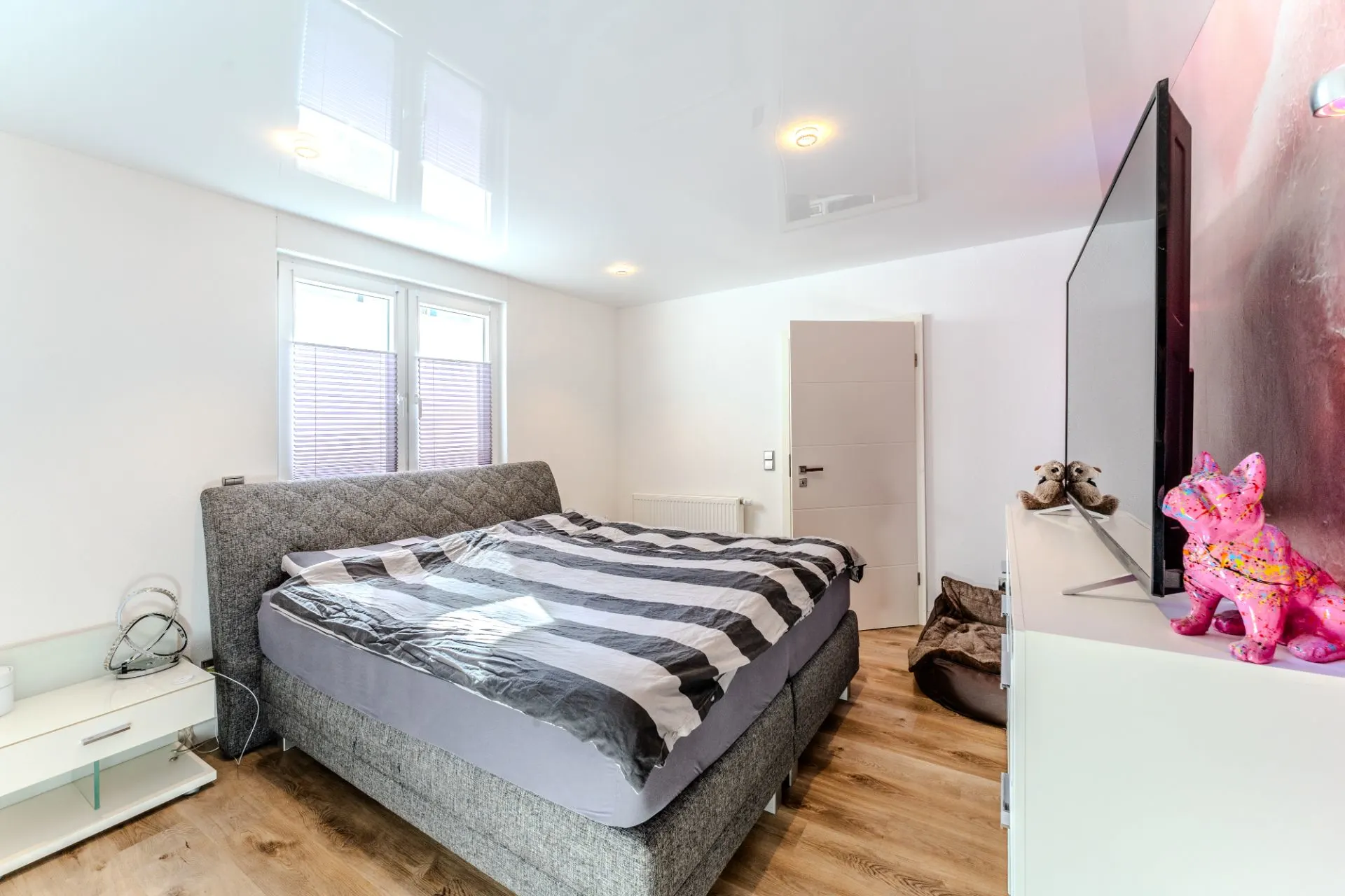Modernes Schlafzimmer mit großem Bett, Fernseher, Nachttisch und Holzfußboden.