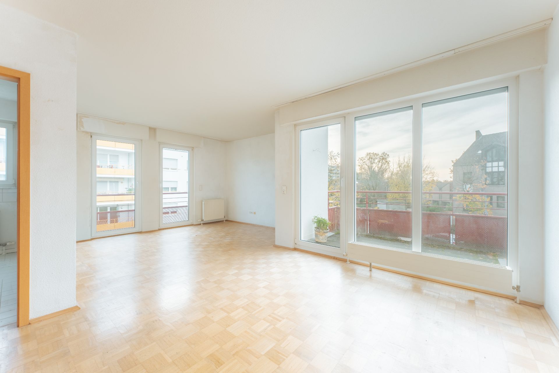 Helles Wohnzimmer mit Parkettboden, großen Fenstern und Zugang zu einem Balkon.