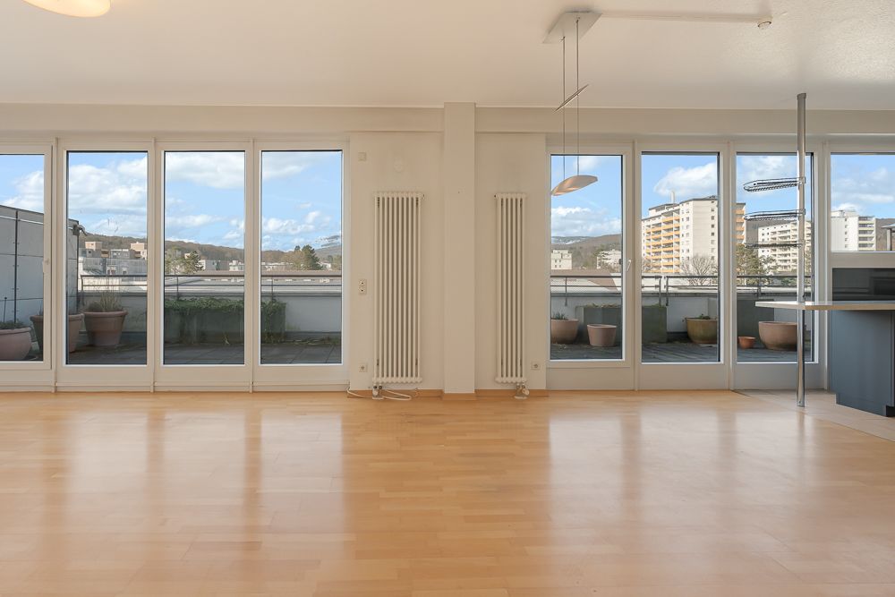Helles Wohnzimmer mit großen Fenstern und Blick auf einen Balkon mit Pflanzenkübeln.