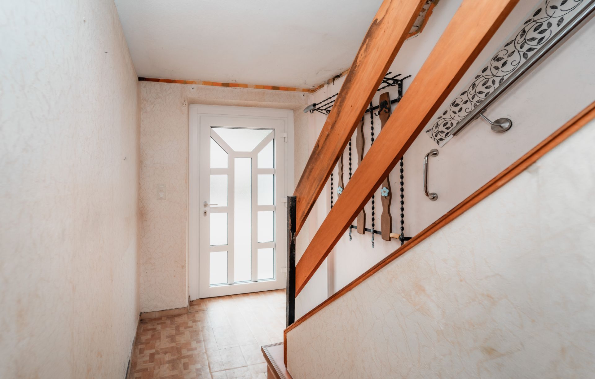 Heller Flur mit Holztreppe und weißer Eingangstür in einem Wohnhaus.
