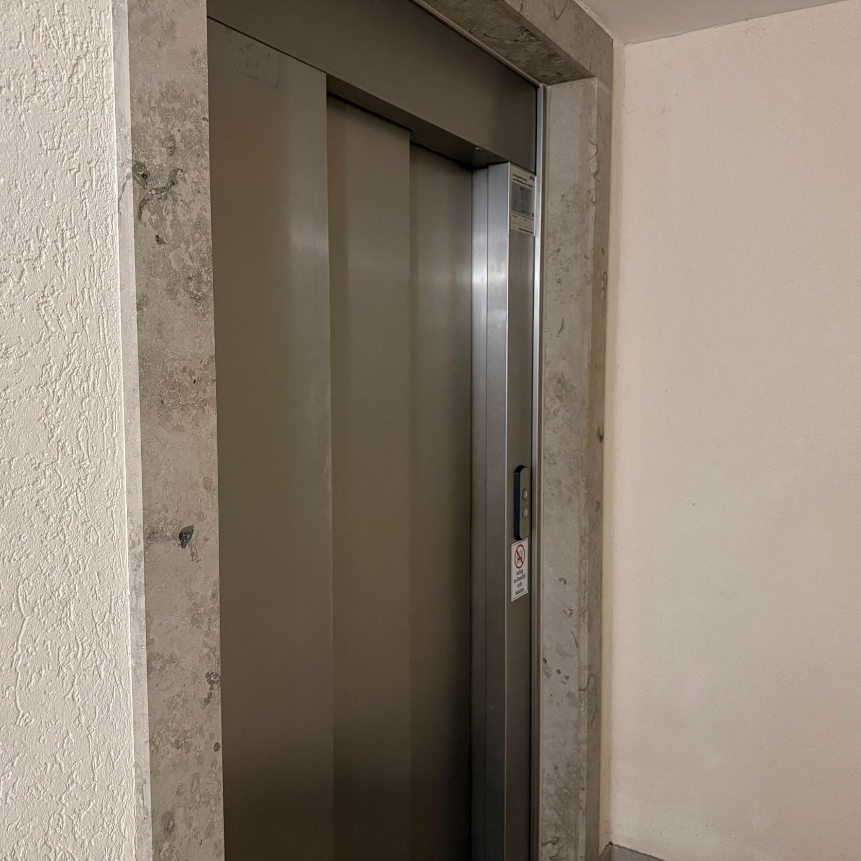 Geschlossene Aufzugtür in einem Wohnhausflur mit hellem Wandputz.