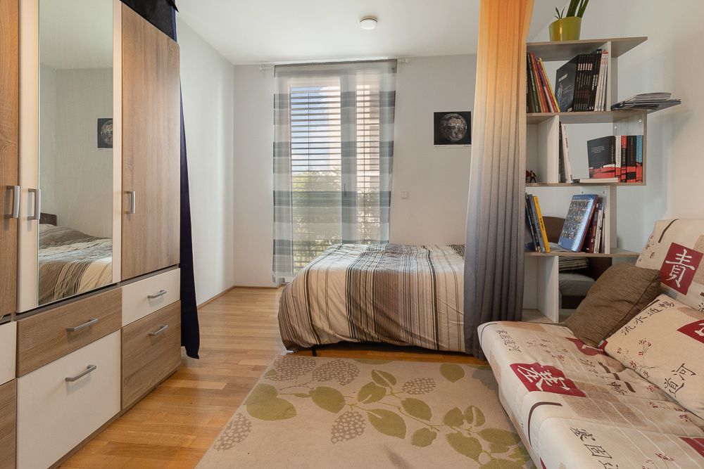 Helles Schlafzimmer mit Bett, Kleiderschrank, Sofa, Regal und großem Fenster.