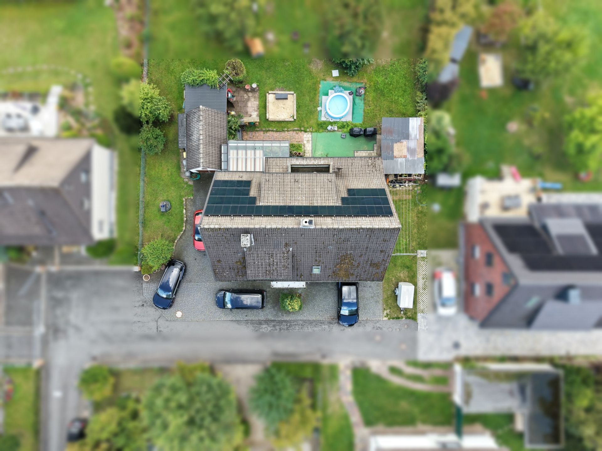 Luftaufnahme eines Hauses mit Garten, Autos und Pool im Hinterhof.