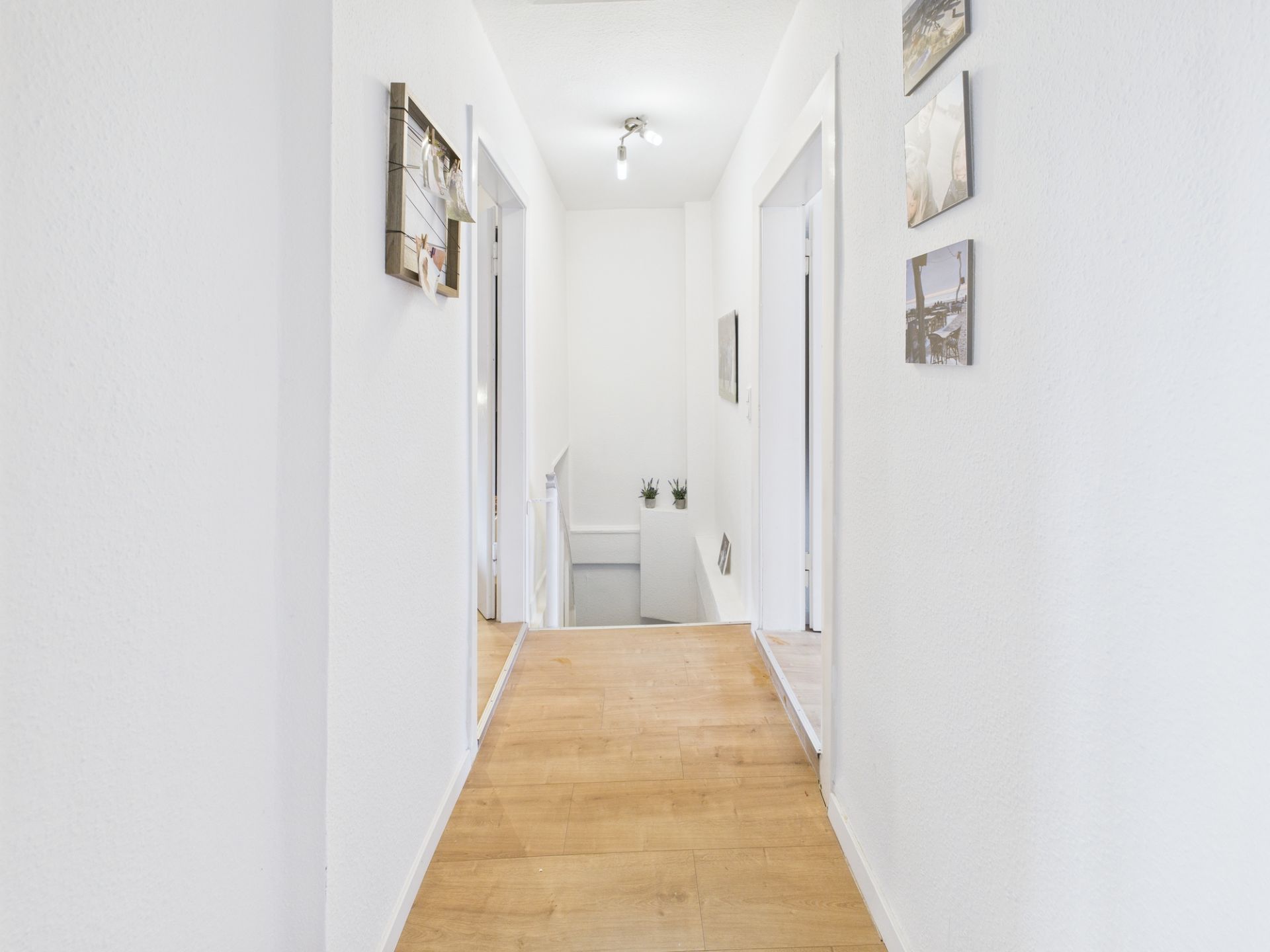 Heller Flur mit Holzfußboden, weißen Wänden und mehreren Türen zu angrenzenden Räumen.