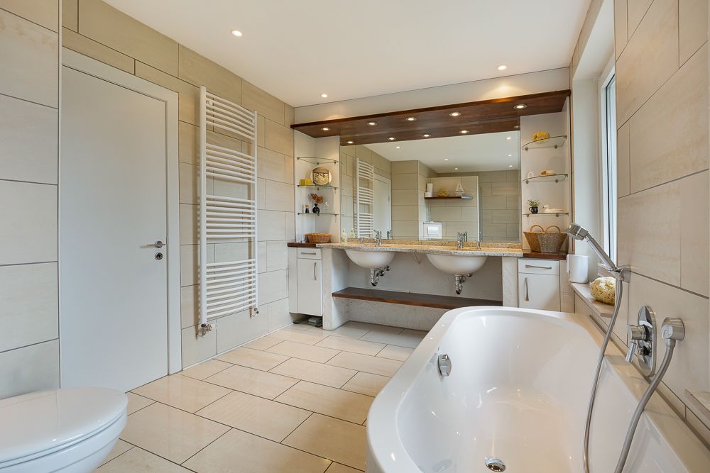 Modernes Badezimmer mit Badewanne, zwei Waschbecken, großem Spiegel und hellen Fliesen.