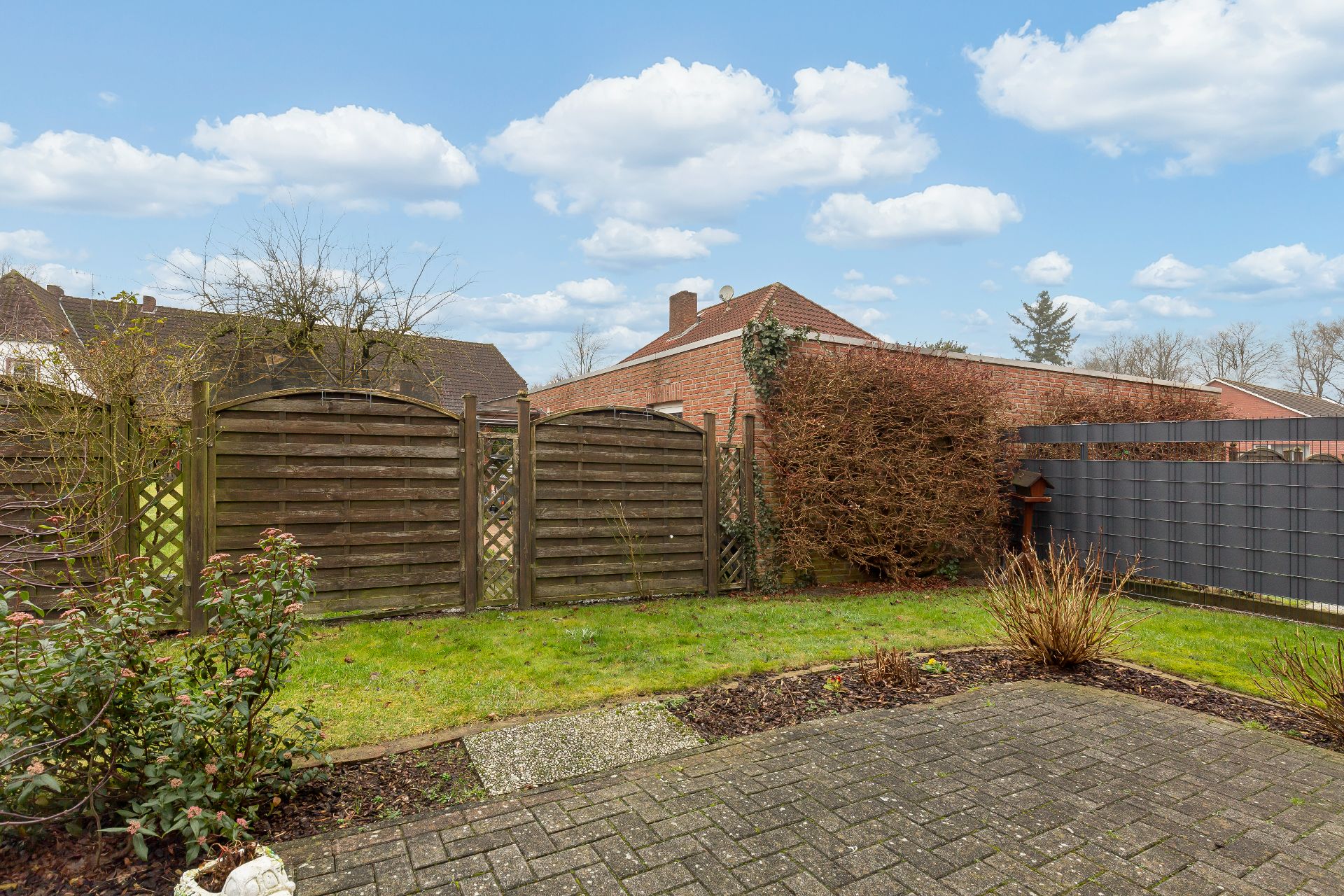 Kleiner Garten mit Rasen, Sträuchern, Terrasse und Holzzaun an einem Wohnhaus.