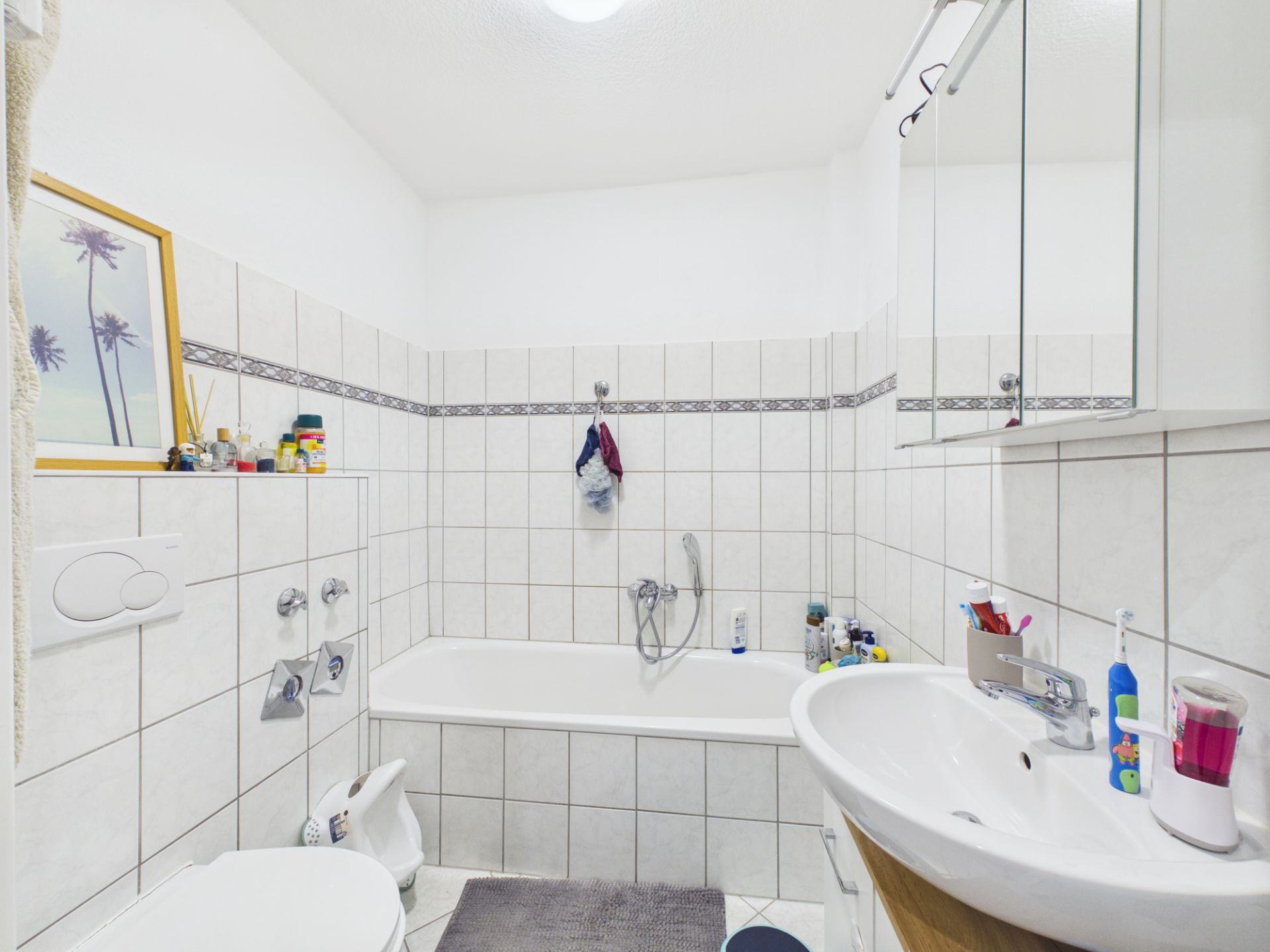 Helles Badezimmer mit Badewanne, Waschbecken, Spiegel und weißen Fliesen.