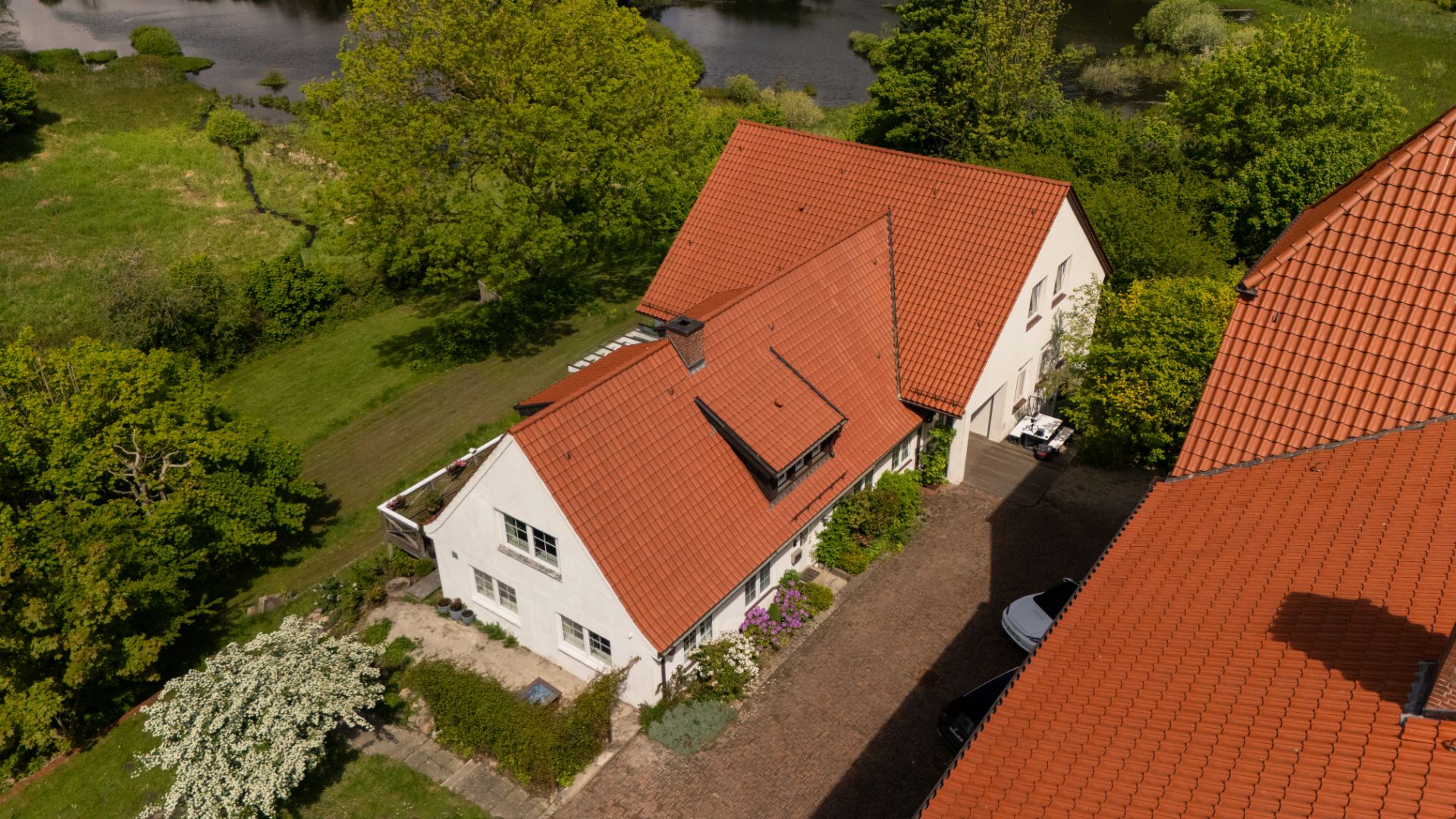 Luftbild von Wohnhaus mit rotem Dach, Garten und Einfahrt, umgeben von Bäumen.