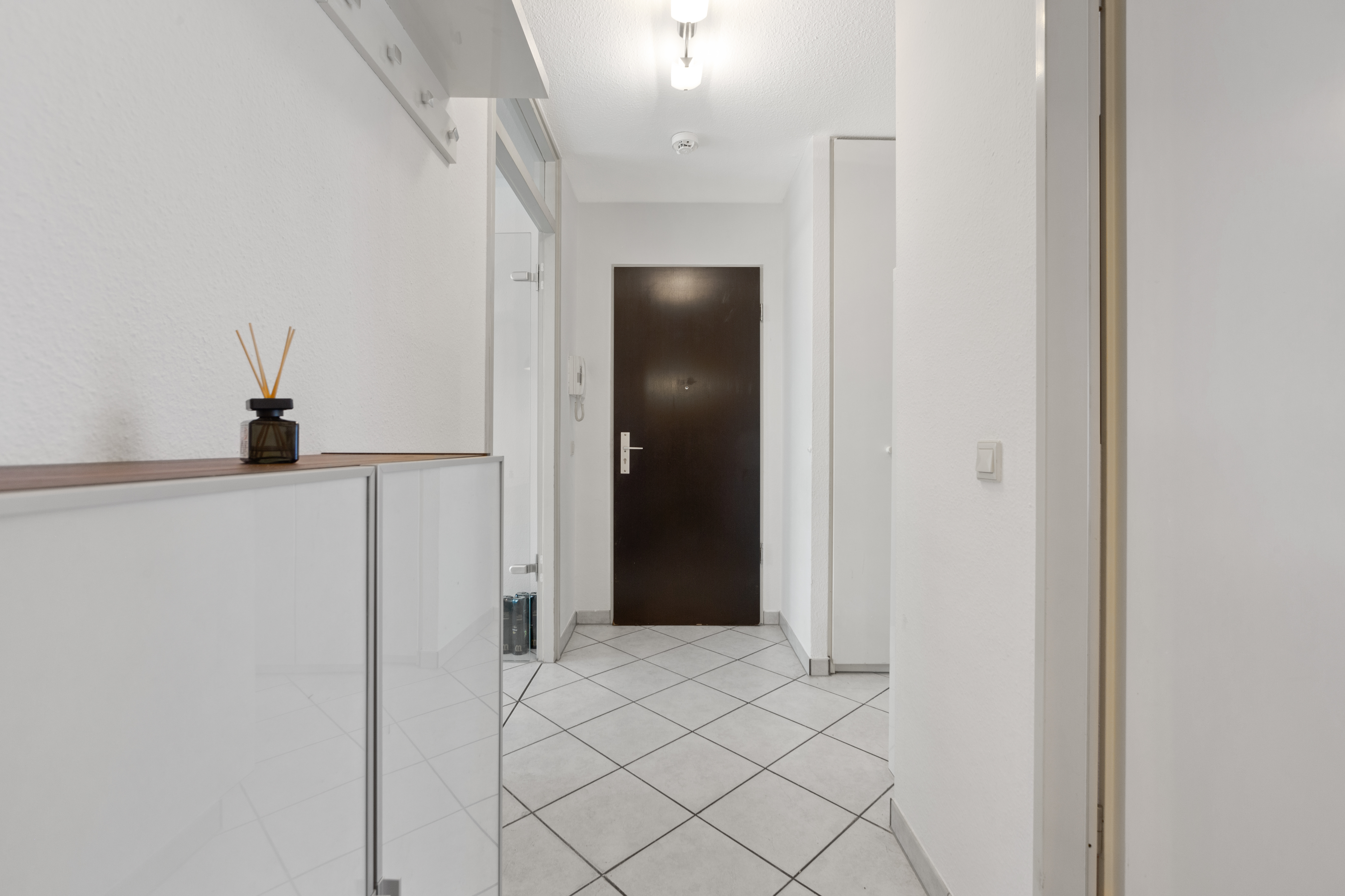 Heller Flur mit weißem Fliesboden, Garderobe, Schuhschrank und dunkler Eingangstür.