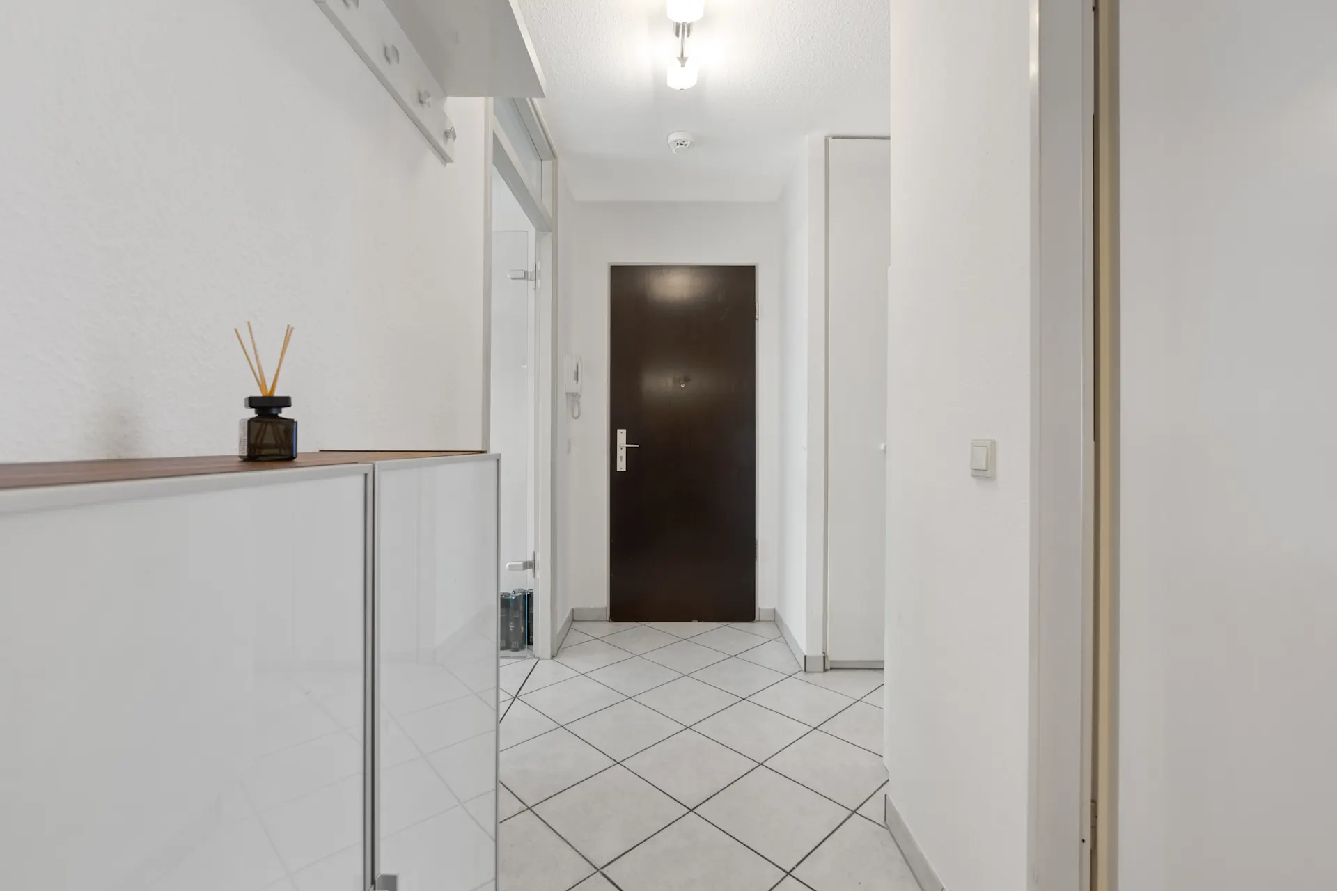 Heller Flur mit weißem Fliesboden, Garderobe, Schuhschrank und dunkler Eingangstür.