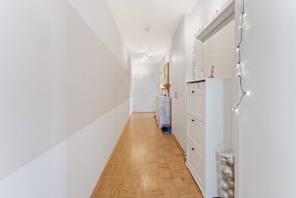 Heller Flur mit Parkettboden, weißen Wänden, Schuhschrank und Lichterkette an der Wand.