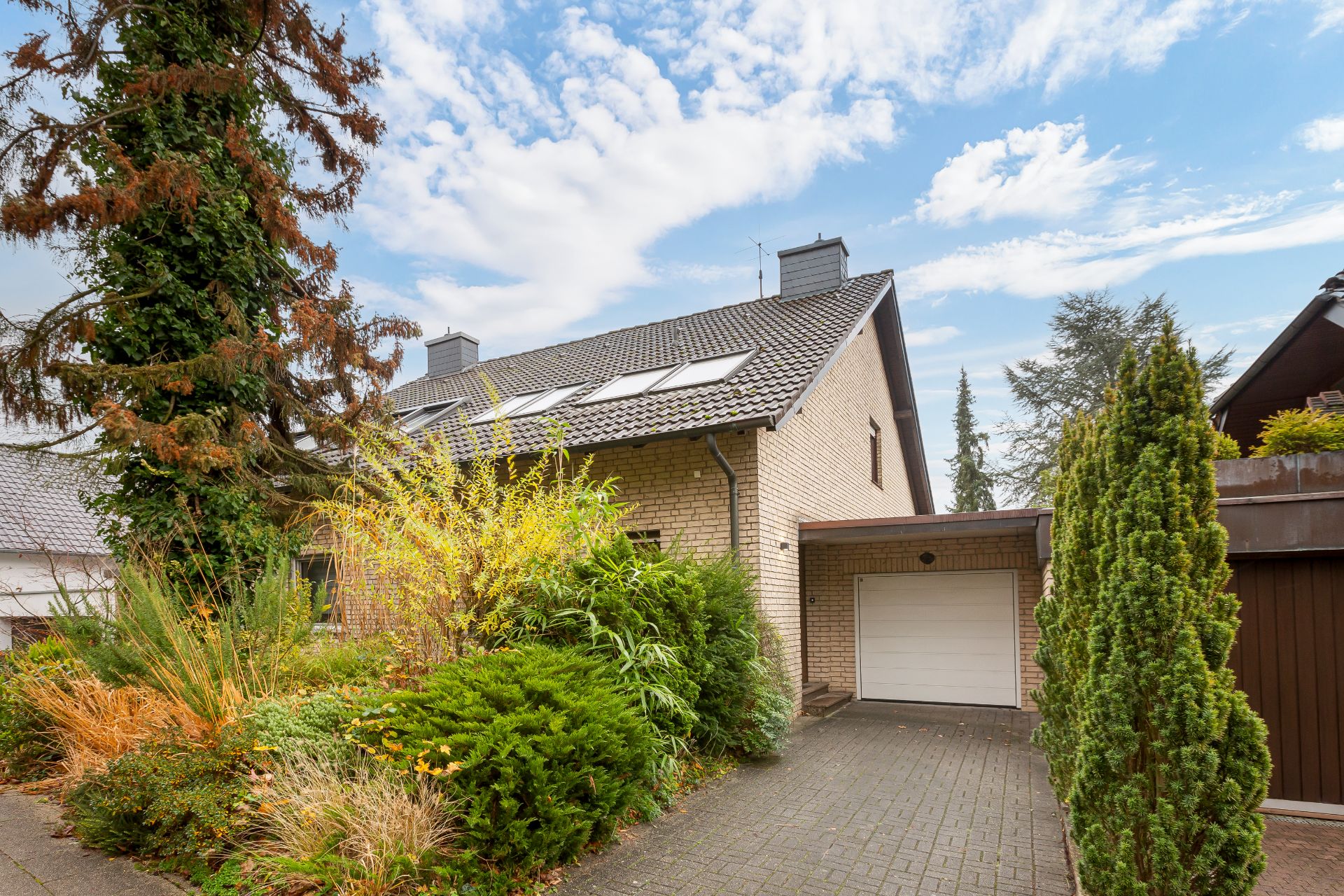 Außenansicht eines Hauses mit Garage, Einfahrt und Garten mit verschiedenen Pflanzen.
