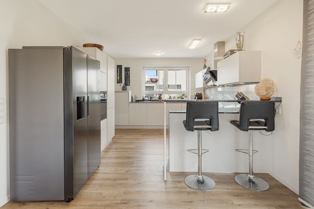 Moderne Küche mit großem Kühlschrank, Kochinsel und zwei Barhockern auf Holzfußboden.