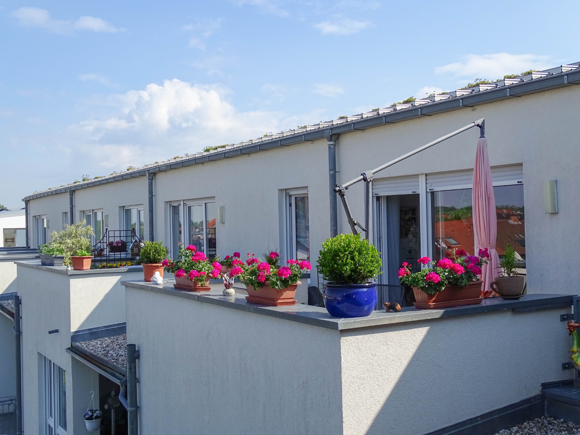Balkon einer Wohnung mit Blumenkästen und einem Sonnenschirm vor weißen Wänden.