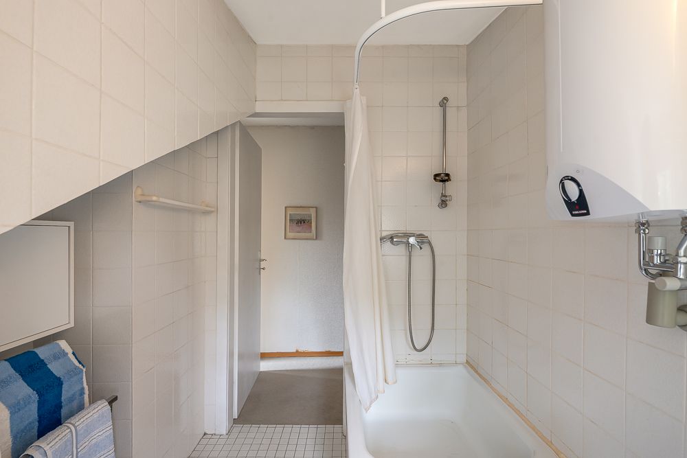 Kleines Badezimmer mit Badewanne, Duschvorhang, Handtüchern und weiß gefliesten Wänden.
