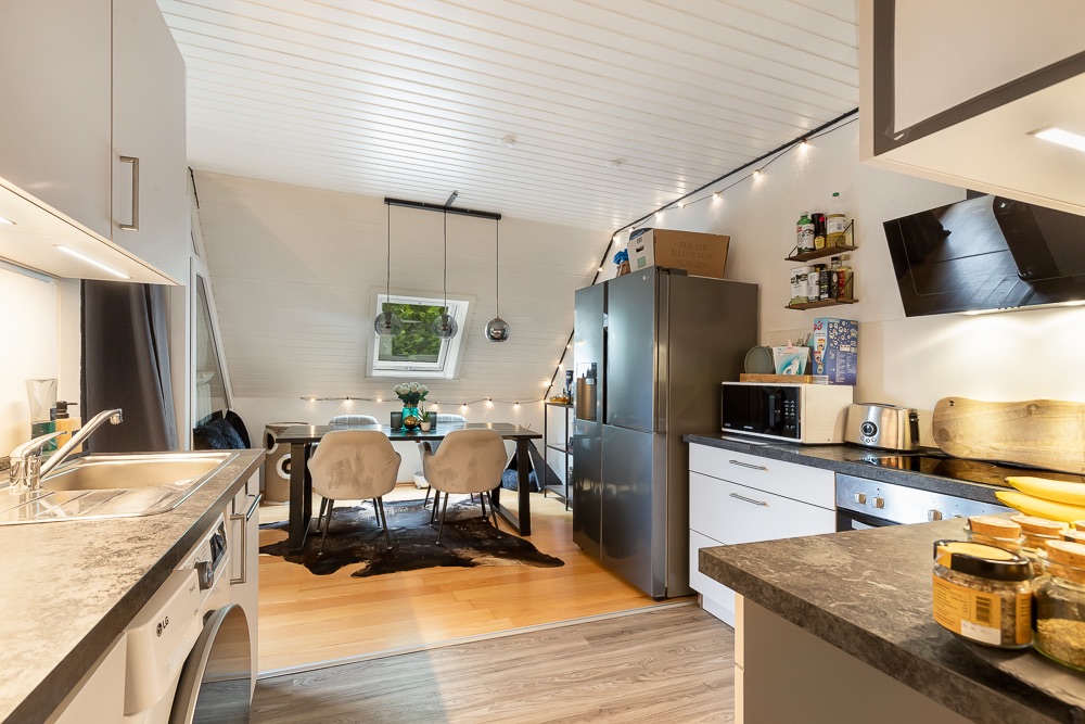 Moderne Küche mit Esstisch, vier Stühlen und großem Kühlschrank, helle Holzdecke.