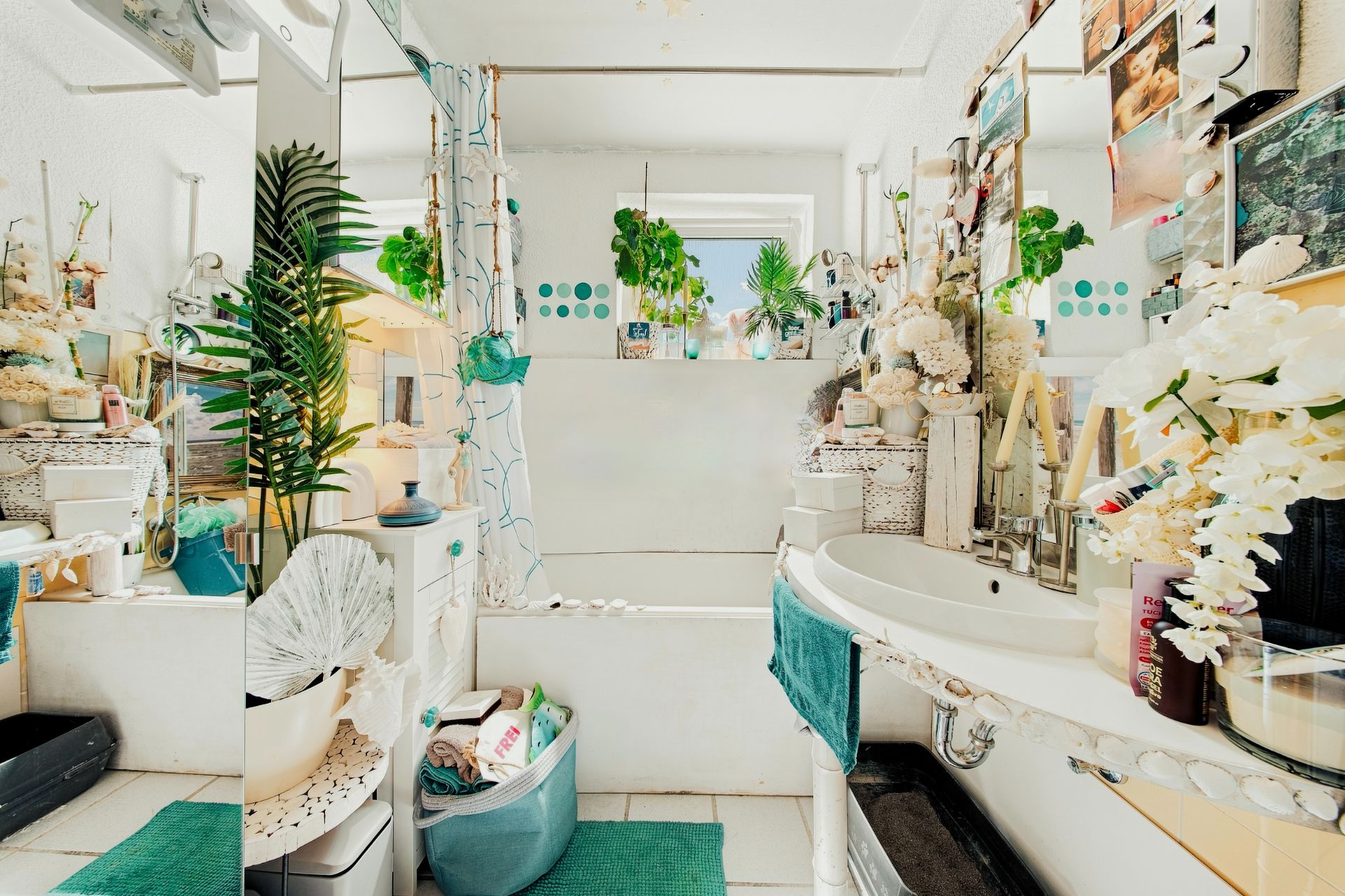 Helles Badezimmer mit Badewanne, Waschbecken, Pflanzen, Spiegel und türkisen Handtüchern.