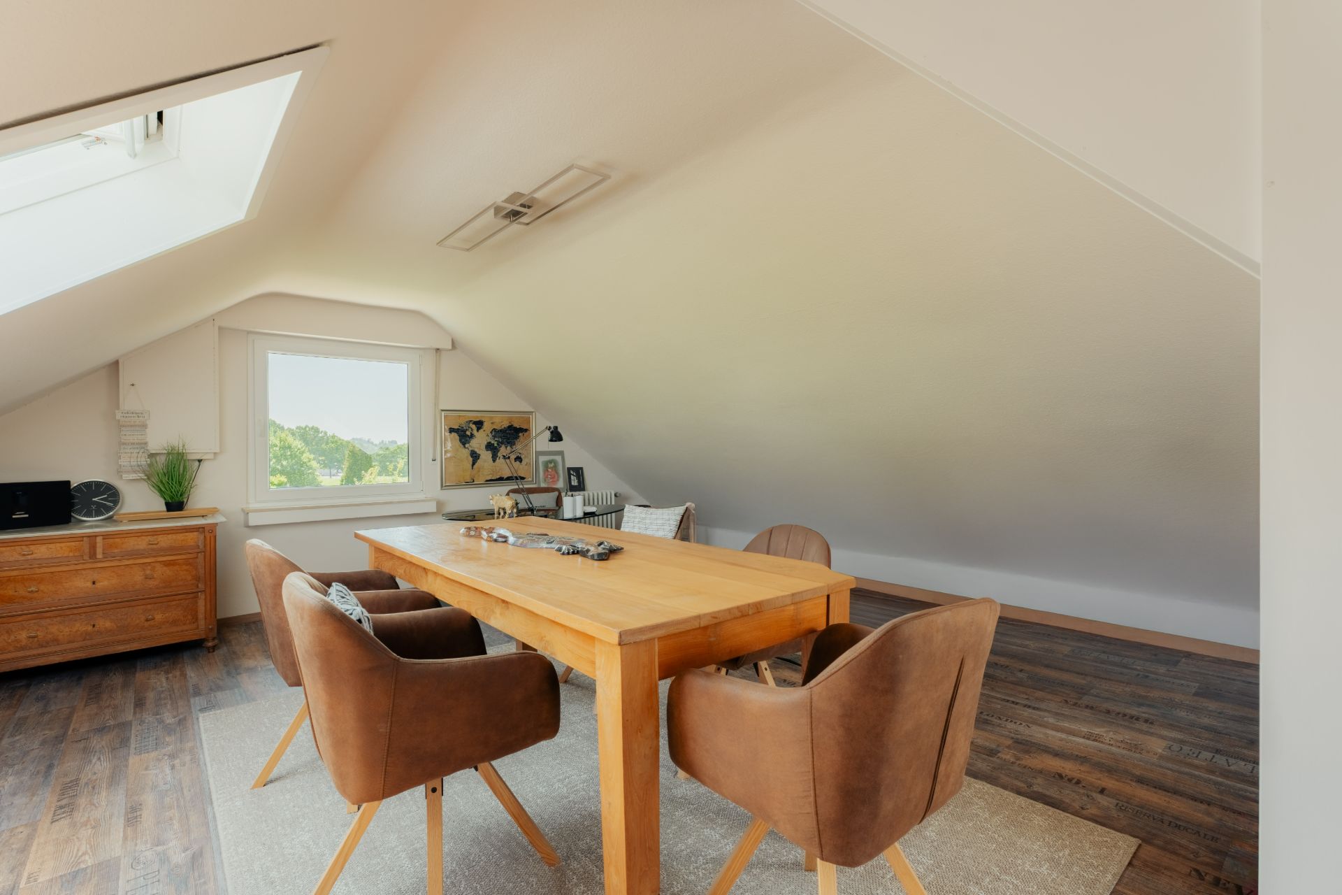 Heller Raum mit schräger Decke, Holztisch, vier Stühlen und Fenster mit Ausblick.