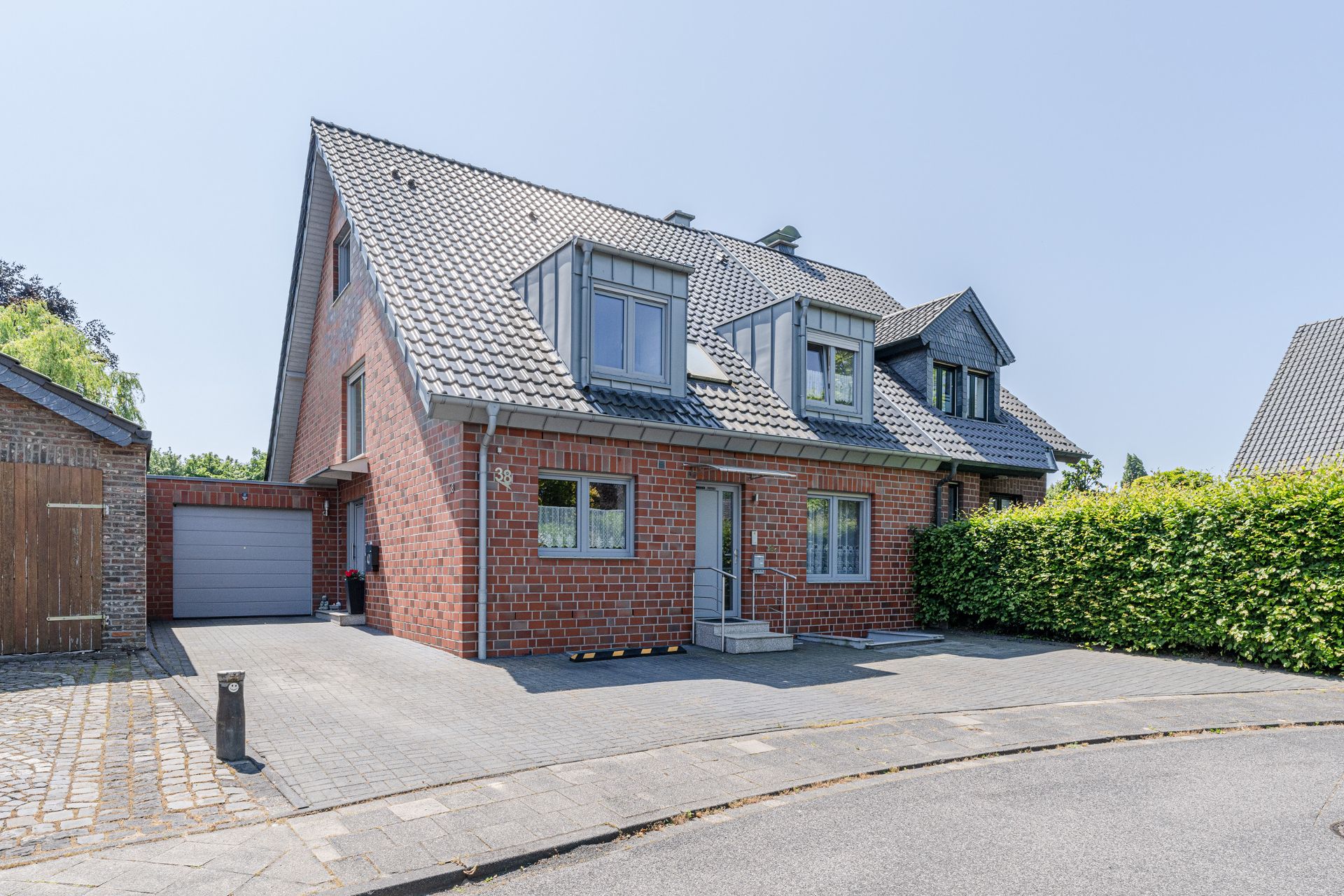 Doppelhaushälfte aus rotem Klinker mit zwei Dachgauben und Garage, davor gepflasterte Einfahrt.