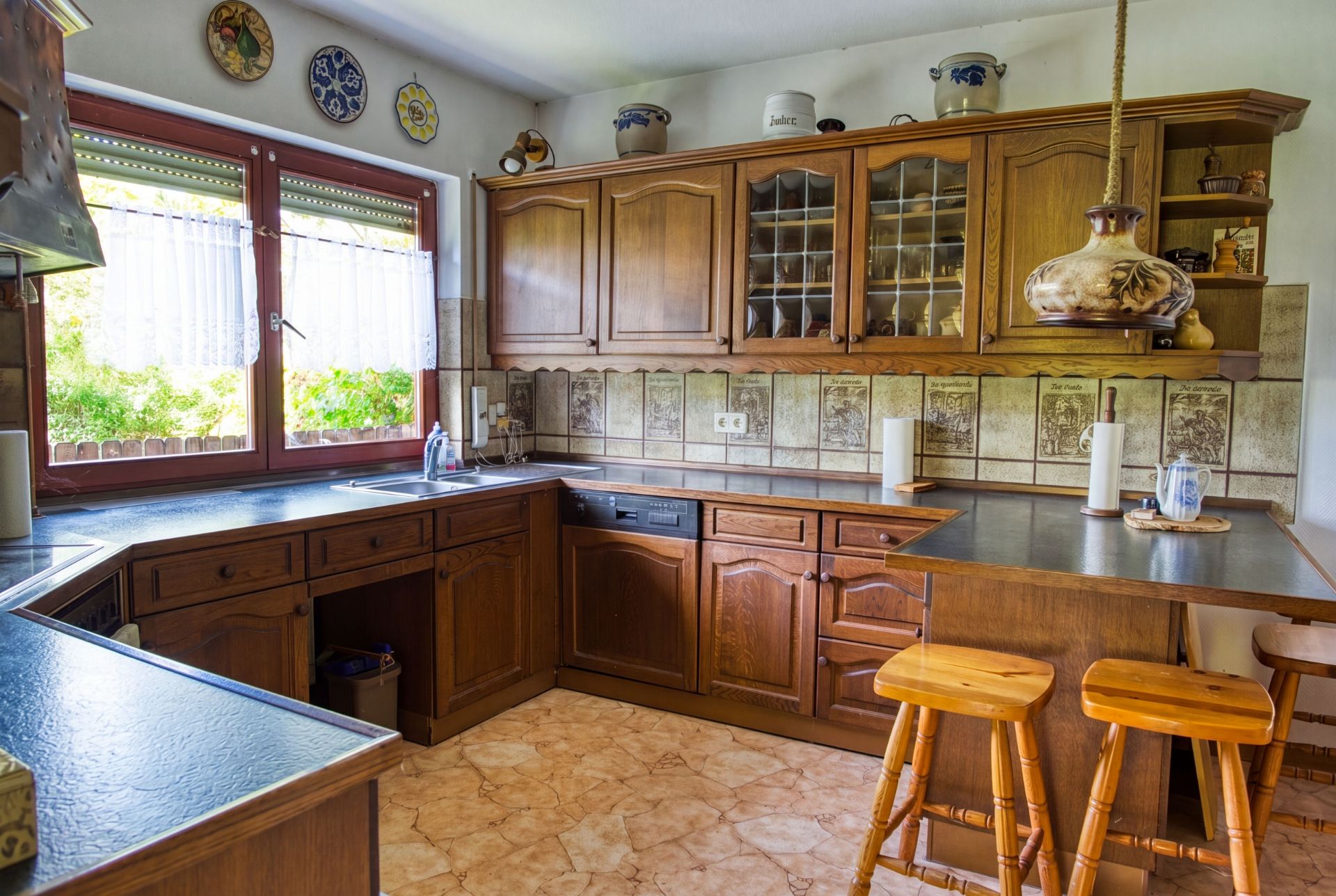 Küche mit Holzmöbeln, großem Fenster, Arbeitsplatten und zwei Holzstühlen an der Theke.