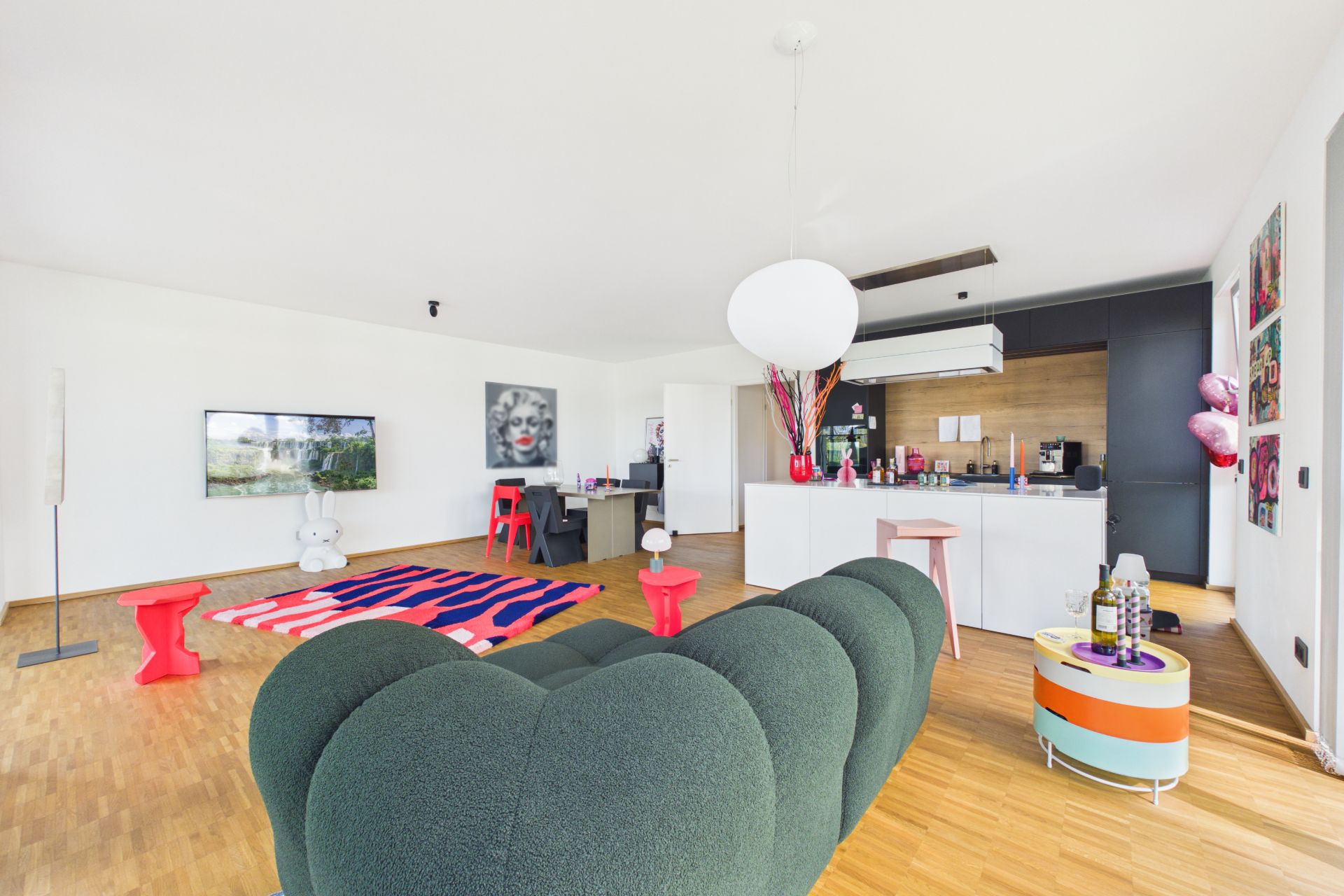 Modernes Wohnzimmer mit grüner Couch, bunter Teppich, offener Küche und Holzboden.