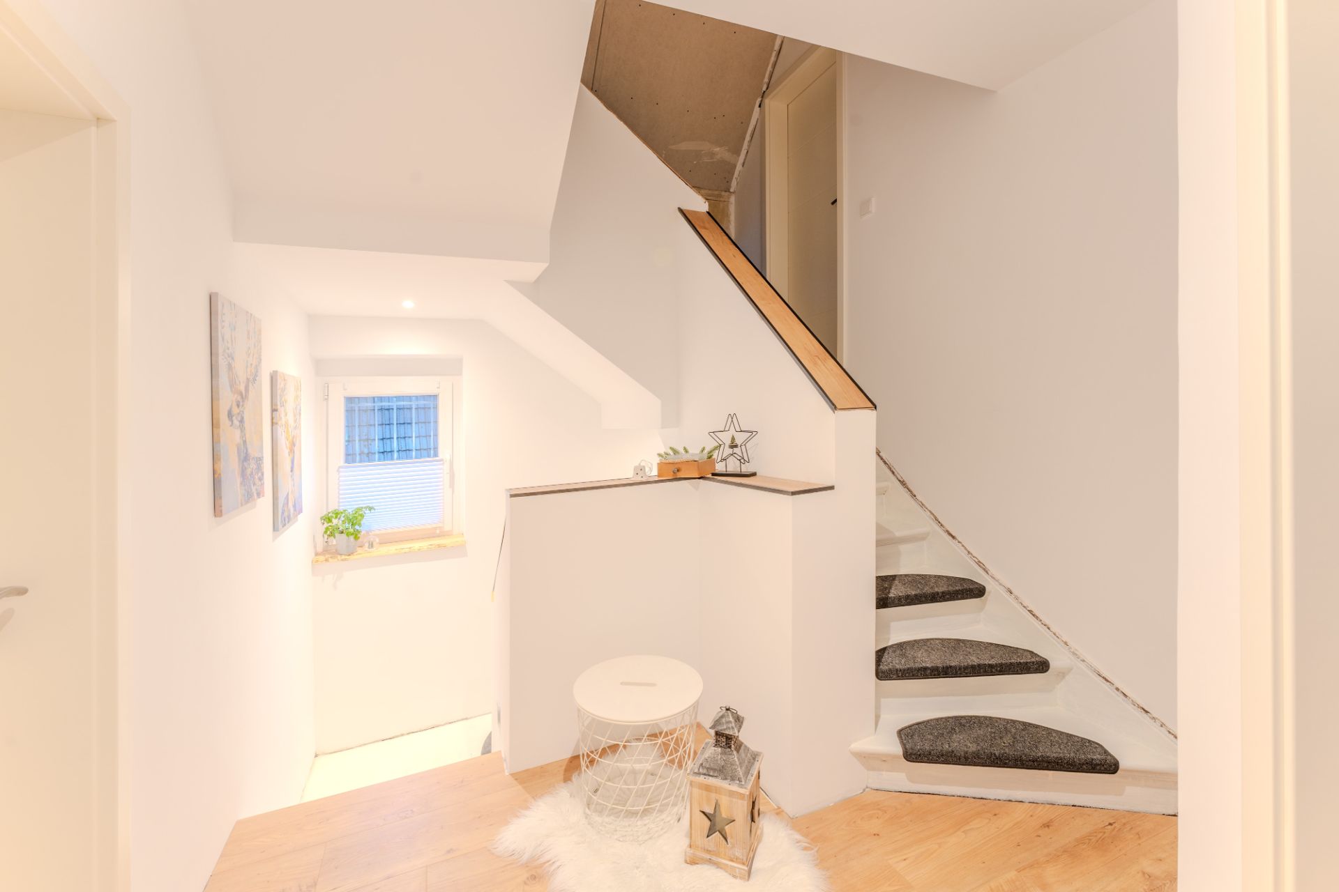 Heller Flur mit Treppe, Fenster, gemalten Bildern und dekorativen Gegenständen.