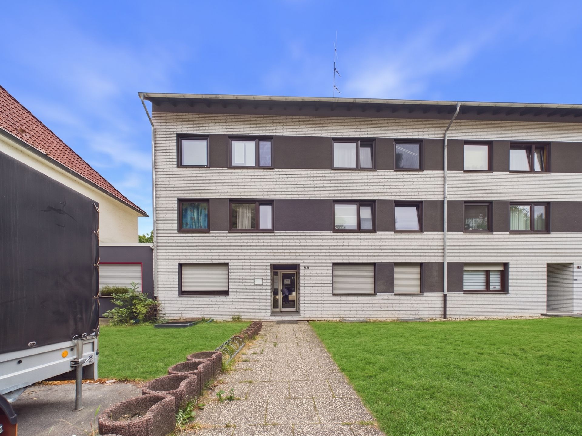Dreistöckiges Wohnhaus mit weißer Fassade, mehreren Fenstern und einem Weg zum Eingang.