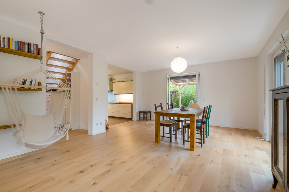 Helles Wohnzimmer mit Holzfußboden, Esstisch, Hängesessel, Bücherregal und Zugang zur Terrasse.