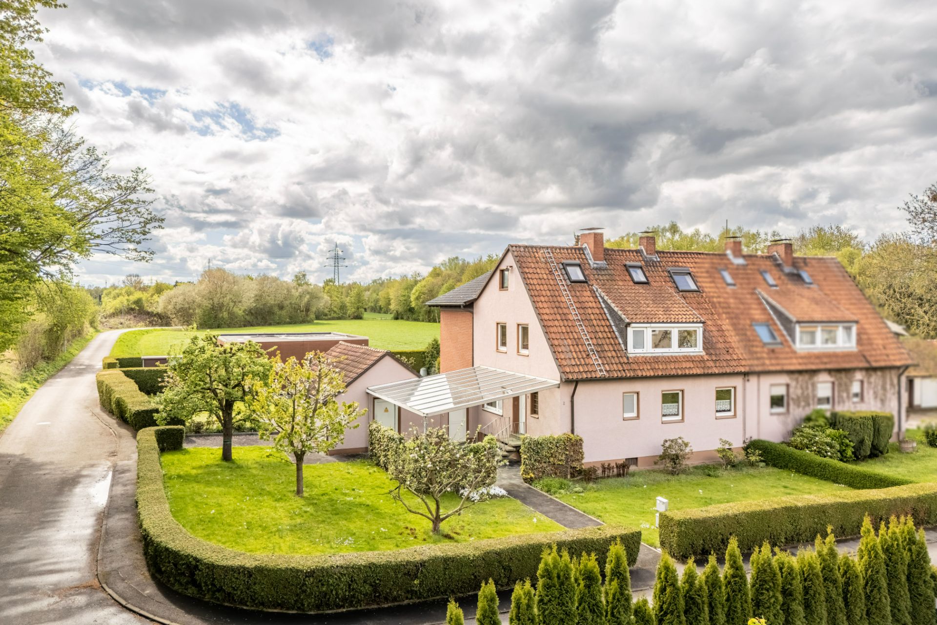 Zweistöckiges Wohnhaus mit rotem Dach und gepflegtem Garten, umgeben von Hecken.