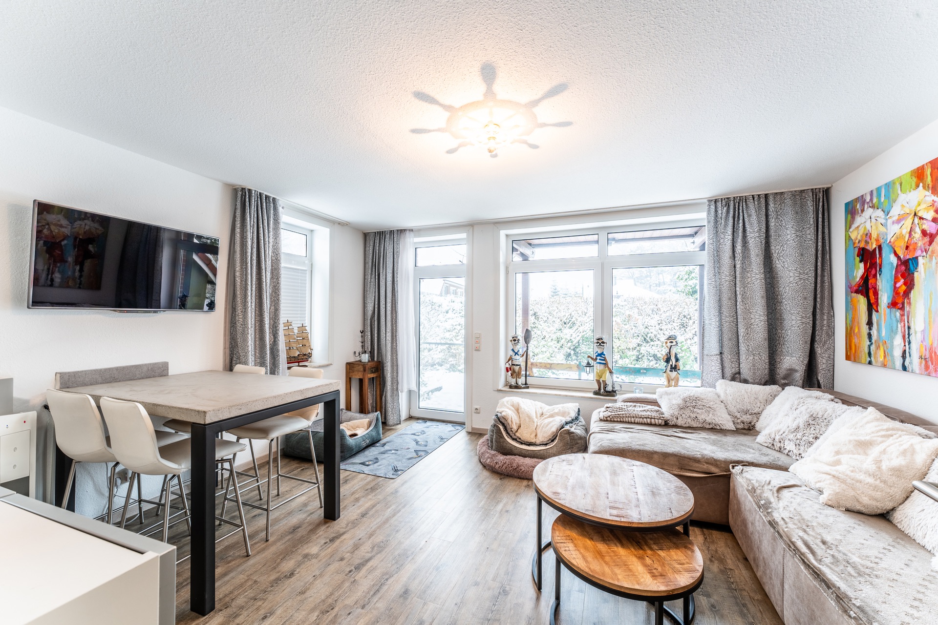 Helles Wohnzimmer mit Ecksofa, Esstisch, Fernseher und großen Fenstern.