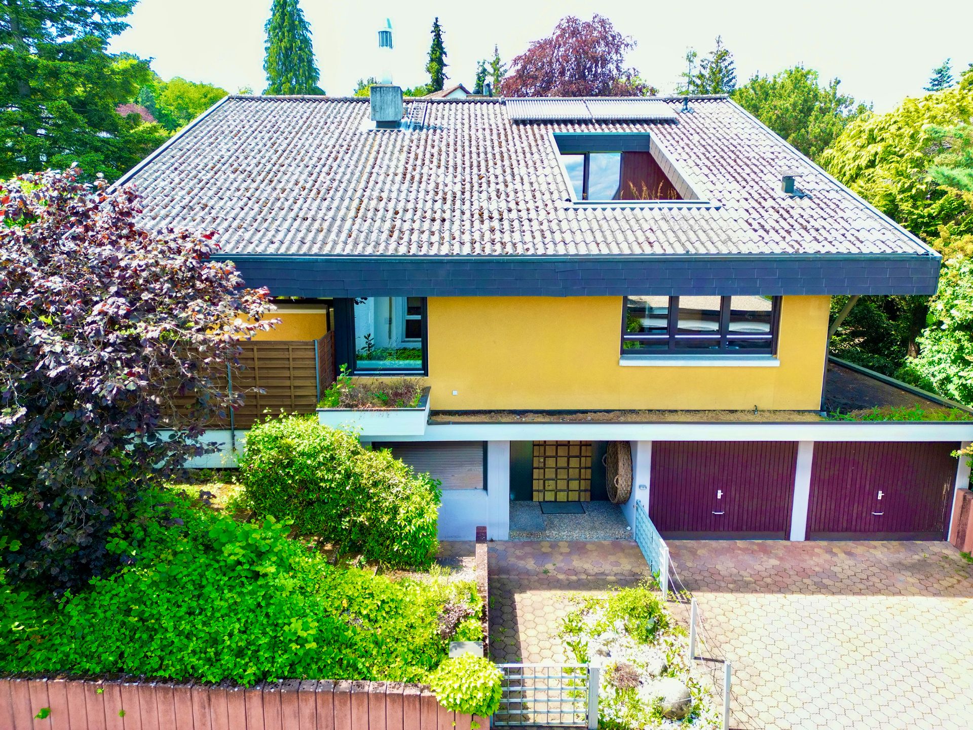 Zweistöckiges Wohnhaus mit gelber Fassade, großem Dach und drei Garagen unterhalb.