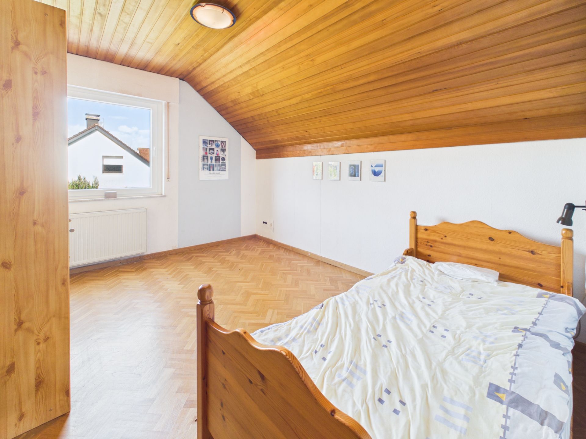 Helles Schlafzimmer mit Holzbett, schräger Holzdecke und großem Fenster.
