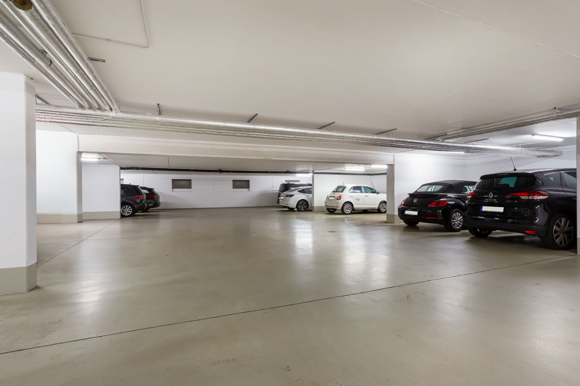 Helle Tiefgarage mit geparkten Autos auf markierten Stellplätzen.
