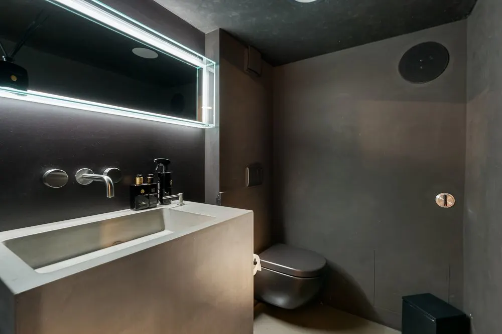 Modernes Badezimmer mit dunkelgrauen Wänden, Waschbecken, Spiegel und Toilette.