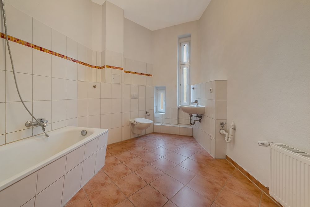 Helles Badezimmer mit Badewanne, WC, Waschbecken, Fenster und Fliesenboden.