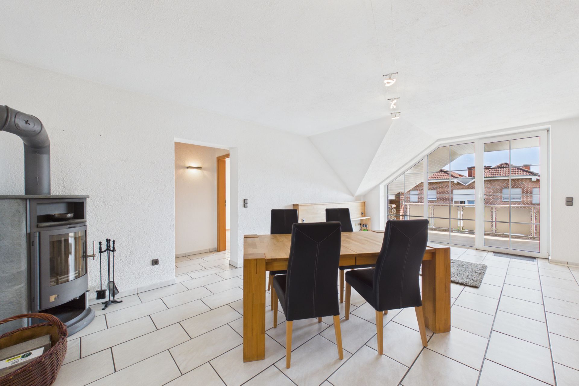 Helles Esszimmer mit Holztisch, vier Stühlen, Kaminofen und Zugang zu einem Balkon.