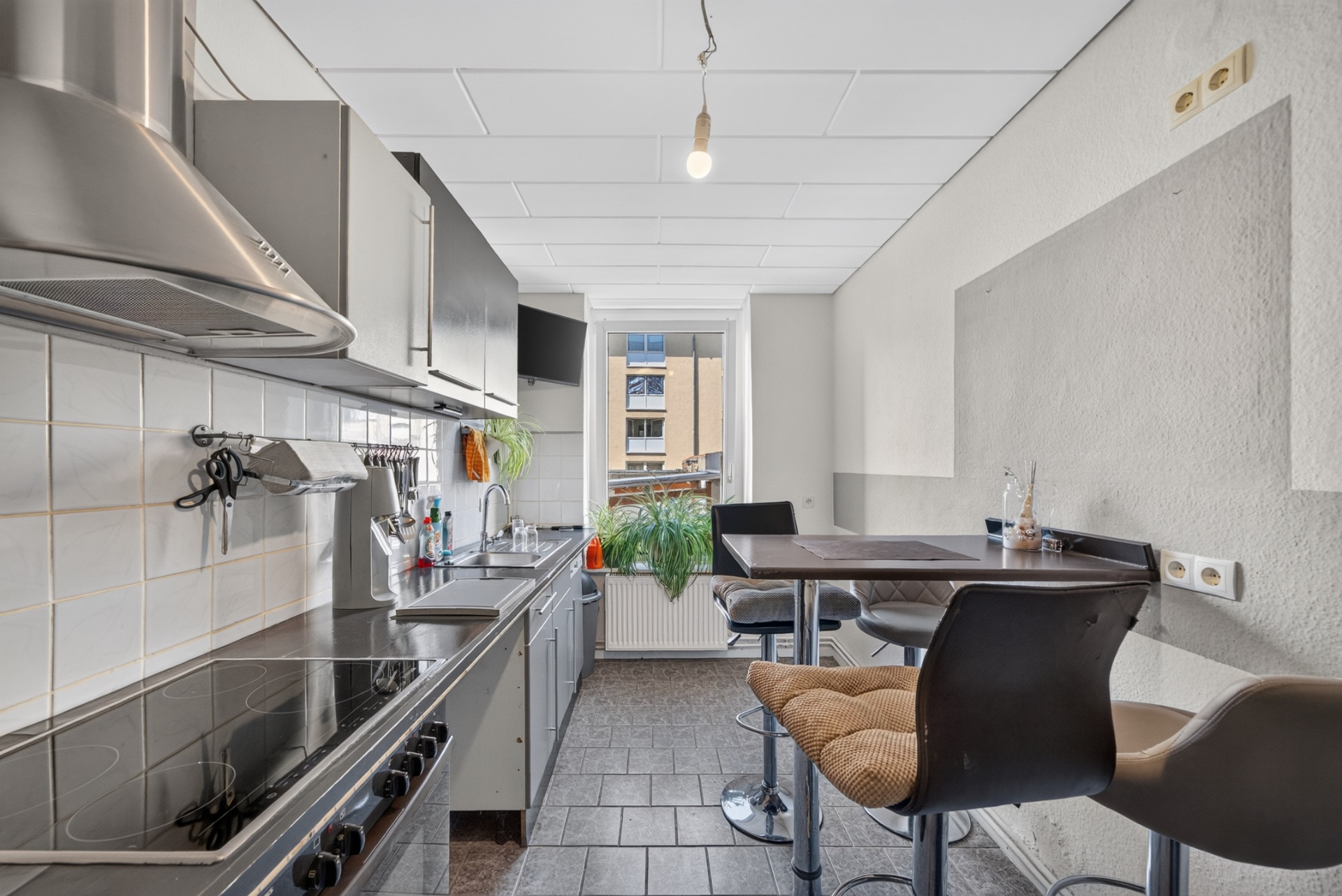 Moderne Küche mit Kochfeld, Spüle, Hängeschränken, Esstisch und Stühlen am Fenster.