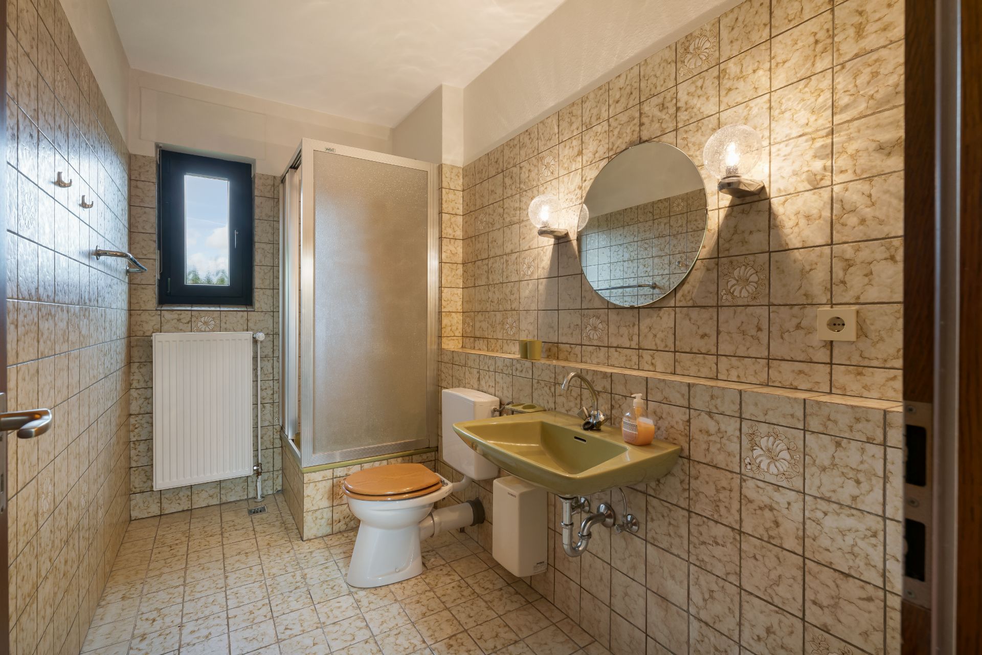 Badezimmer mit Dusche, WC, grünem Waschbecken, Spiegel und Fliesen an den Wänden.