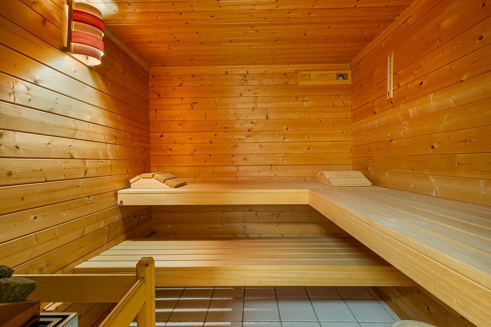 Holzsauna mit zwei Liegeflächen, Lampe an der Wand und weißem Fliesenboden.