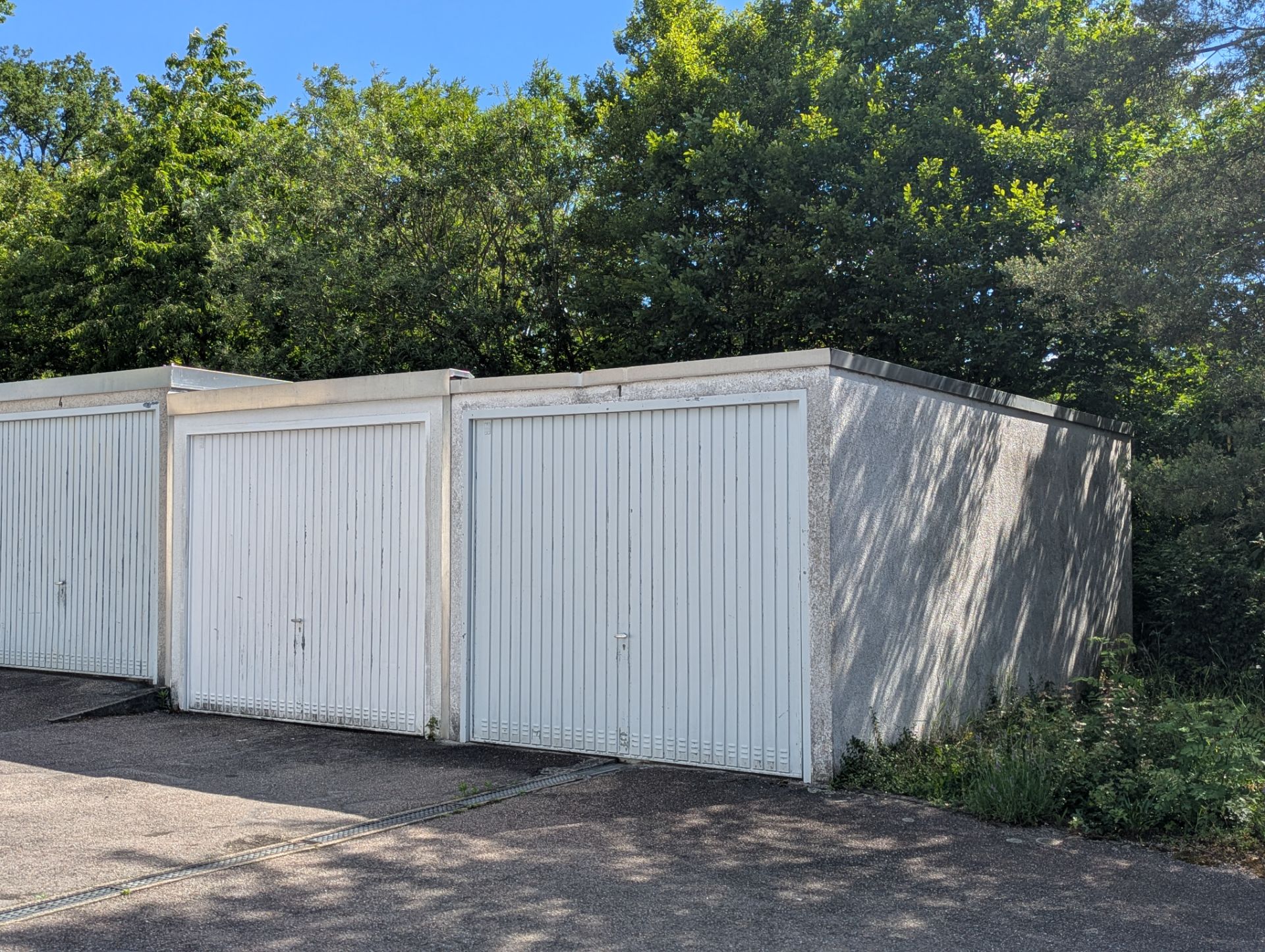Zwei weiße Garagen mit geschlossenen Toren stehen nebeneinander vor Bäumen.
