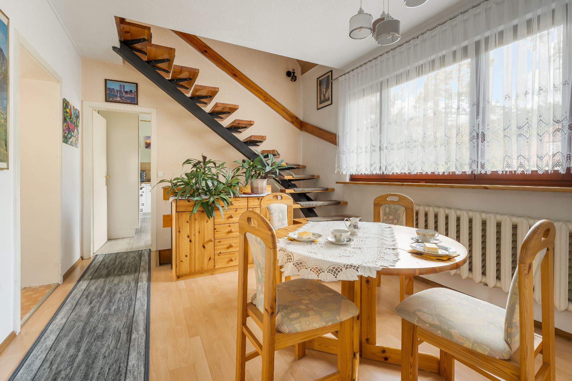 Essbereich mit Holztisch, Stühlen, Topfpflanzen und offener Holztreppe neben großem Fenster.