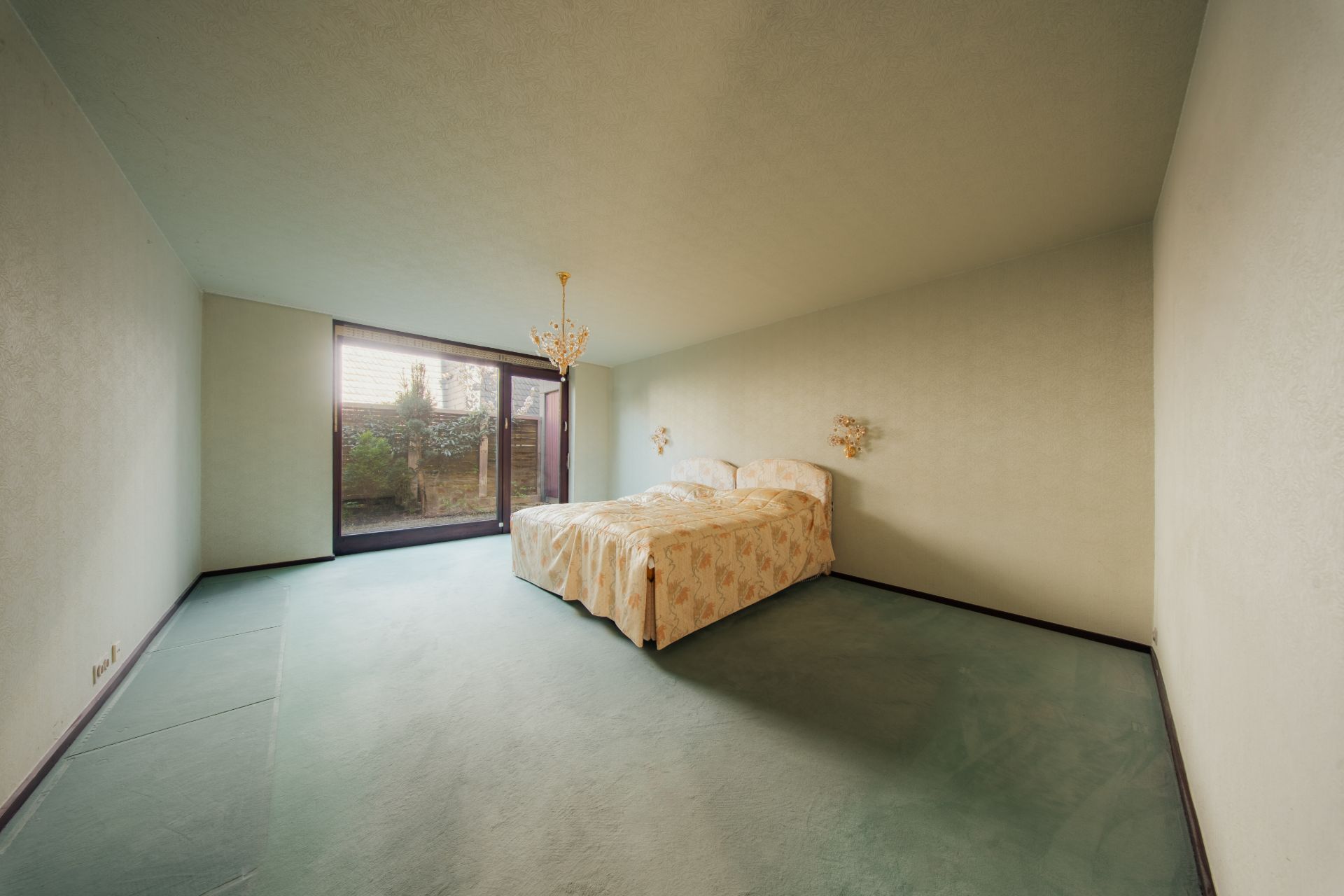 Schlafzimmer mit Doppelbett, großem Fenster und grünem Teppichboden.