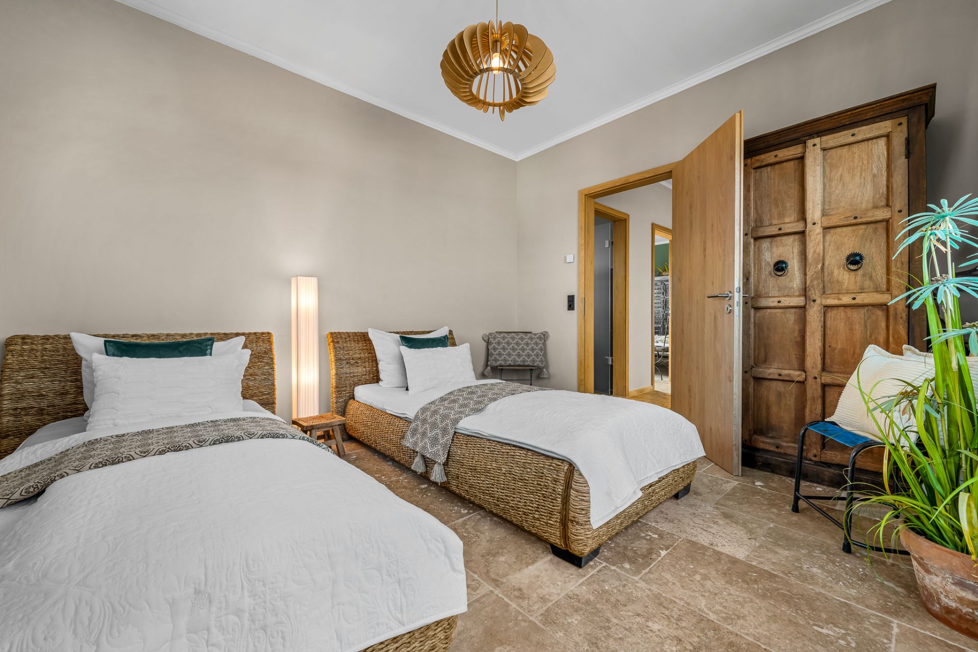 Schlafzimmer mit zwei Einzelbetten, Holzschrank, Pflanze und Lampe.