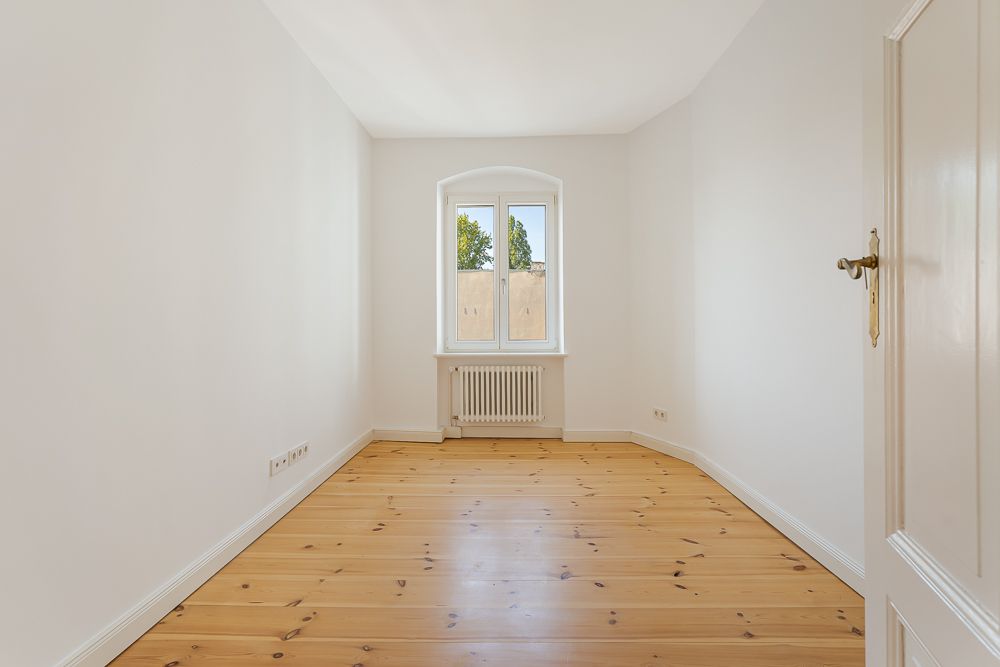Leeres Zimmer mit Holzboden, weiß gestrichenen Wänden und Fenster mit Blick nach draußen.