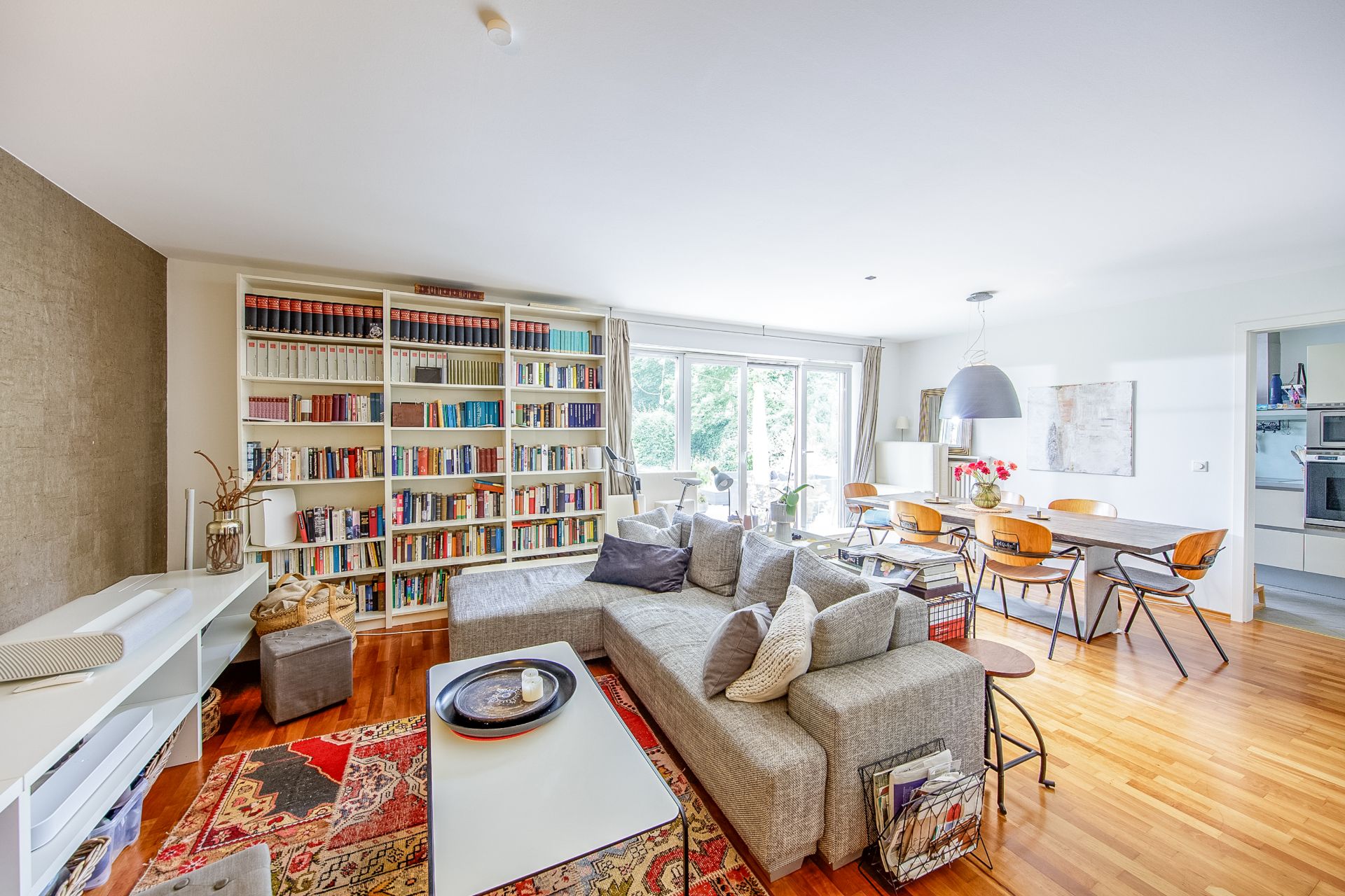Helles Wohnzimmer mit großer Couch, Bücherregal, Esstisch und Blick auf den Garten.