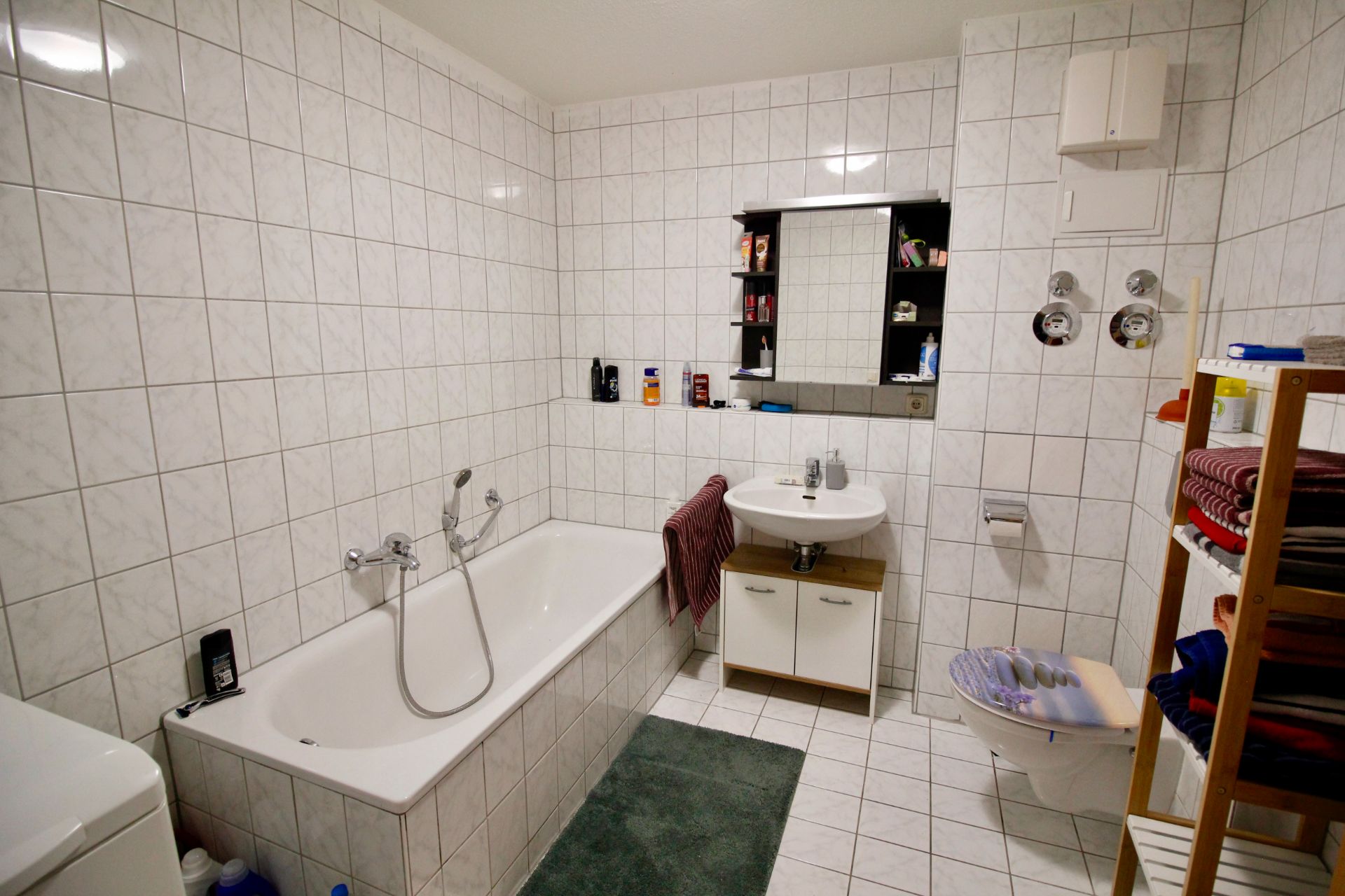 Badezimmer mit Badewanne, Waschbecken, Spiegel, Toilette und Regal mit Handtüchern.