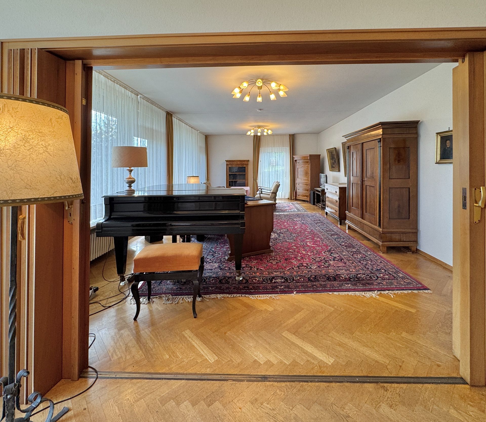 Großes Wohnzimmer mit Flügel, Teppich, Holzmöbeln und großen Fenstern.