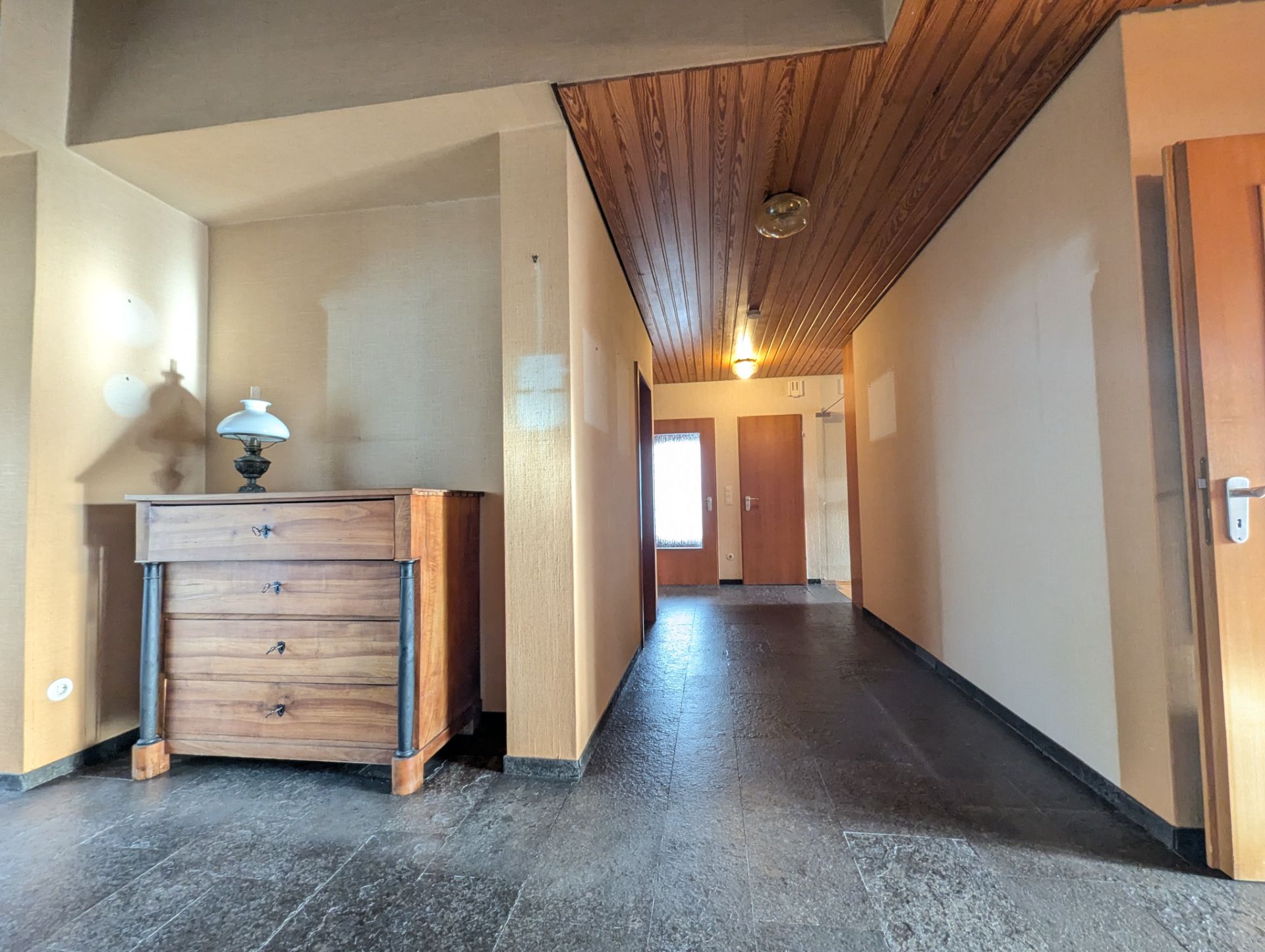 Flur mit Holzdecke, Kommode mit Lampe und mehreren Türen.