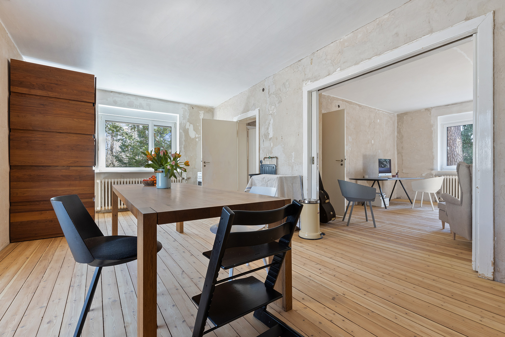 Helles Zimmer mit Holzboden, Esstisch, Stühlen und angrenzendem Arbeitsbereich.